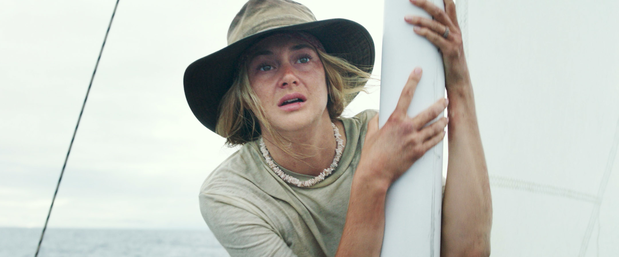 A person in a wide-brimmed hat clings to a sail, appearing distressed, in a scene likely from a movie or TV show