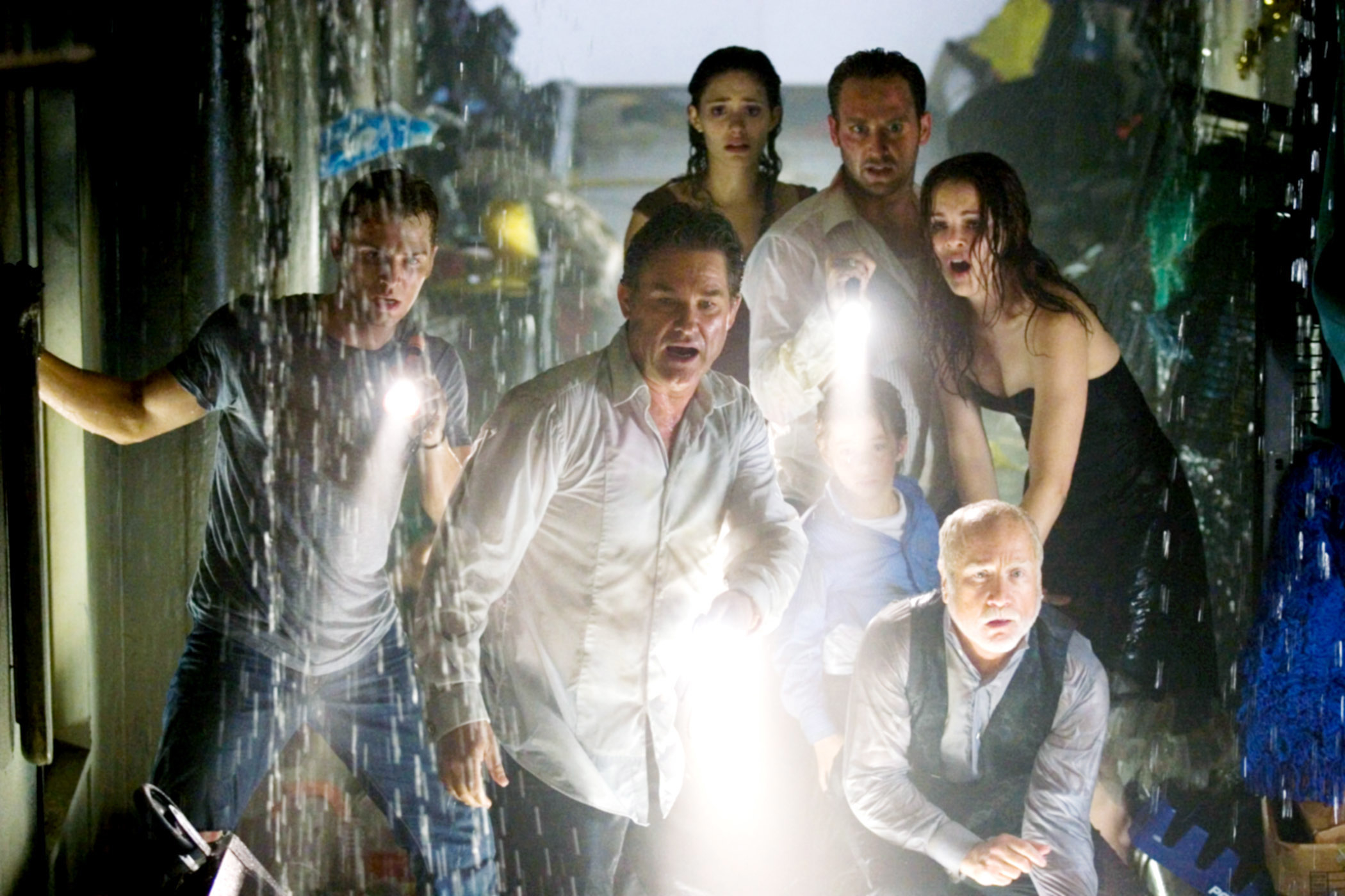 Scene from a movie with several people appearing distressed and wet, holding flashlights, amidst falling water
