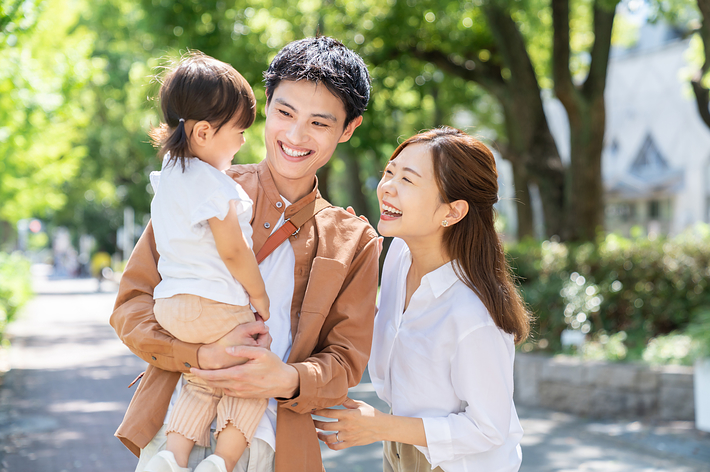 画像には、人々の名前はありませんが、若い家族が公園で微笑んでいます。親が子供を抱いています。