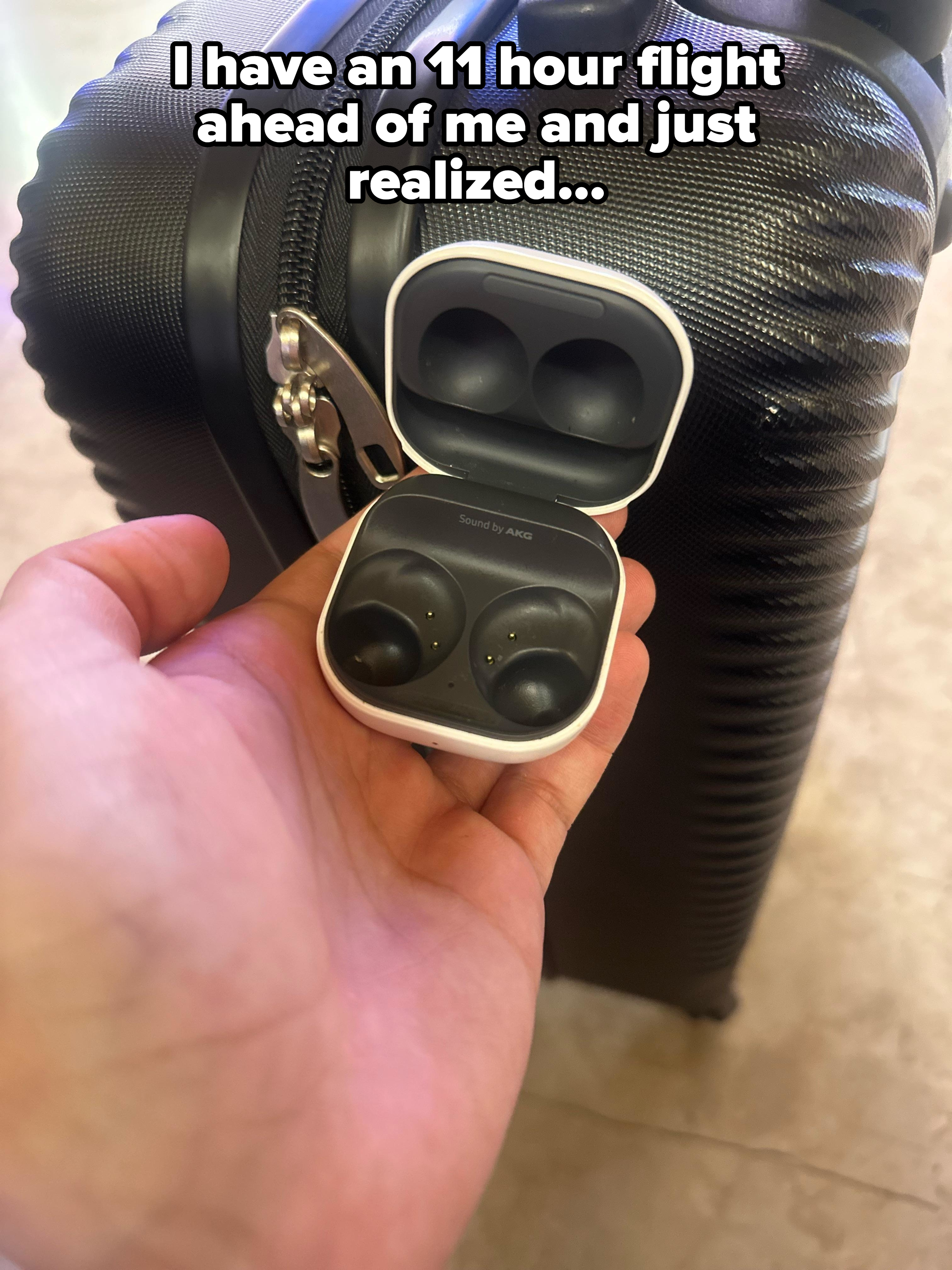 Hand holds open case of wireless earbuds labeled &quot;Sound by AKG&quot; in front of a textured suitcase