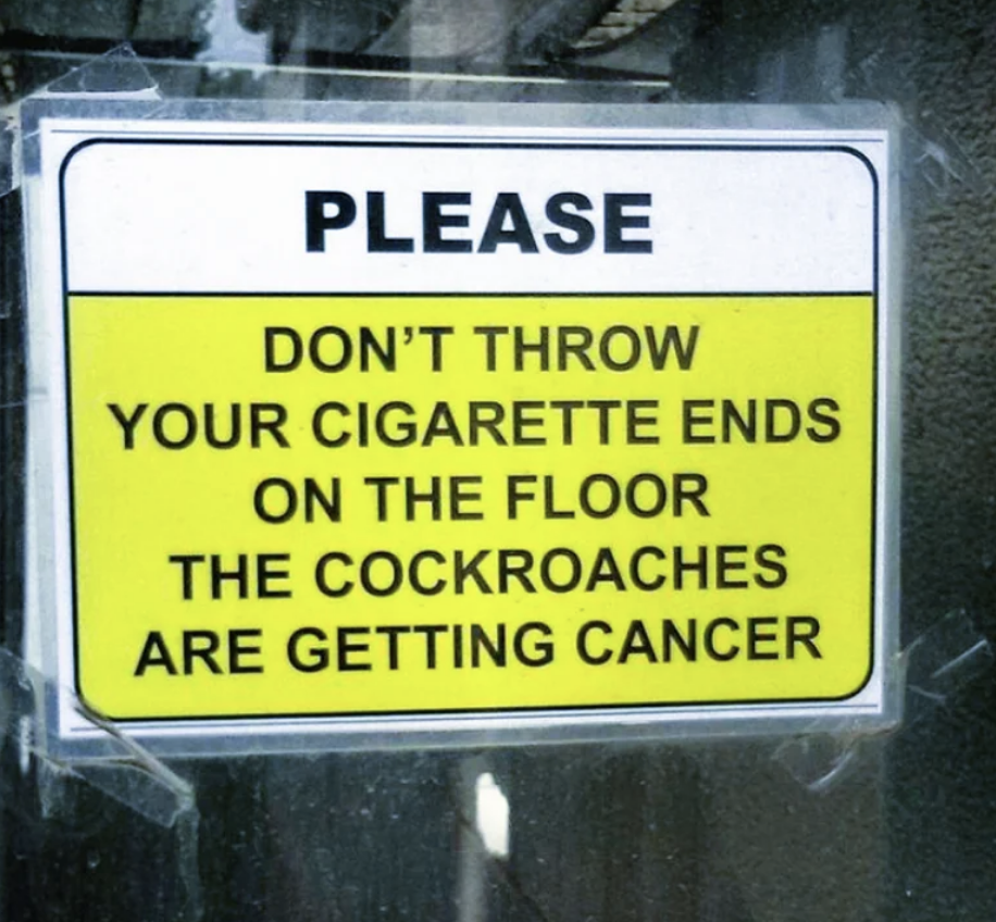 Sign humorously warns against littering cigarette ends, claiming it causes cancer in cockroaches