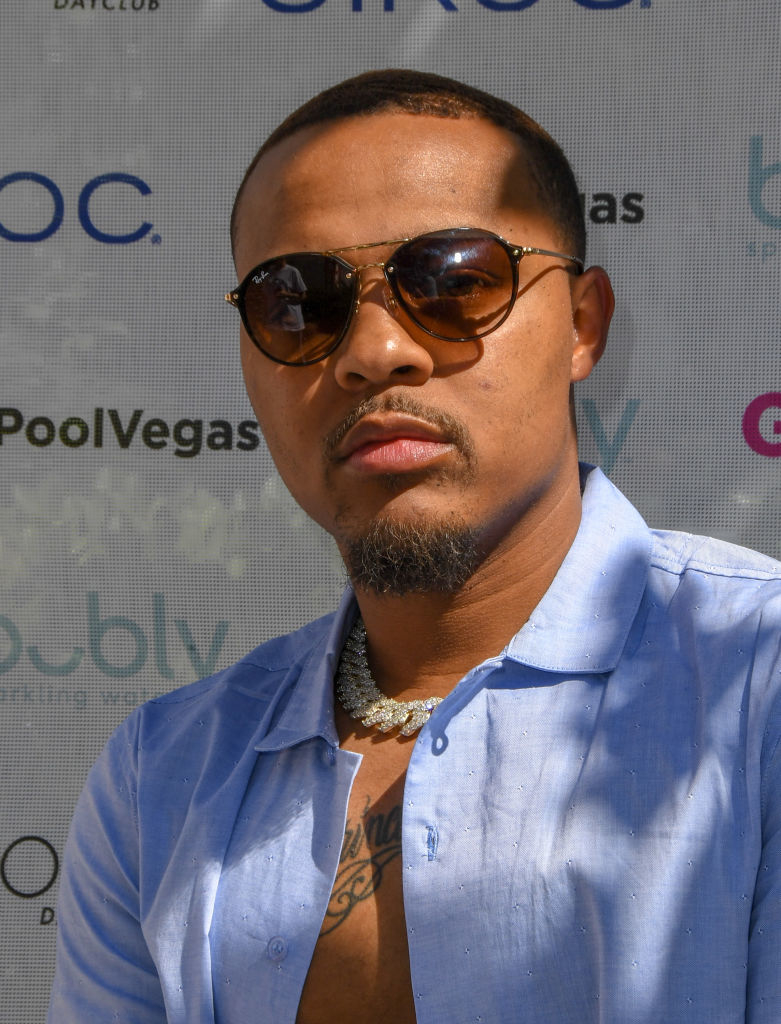 A person in sunglasses and a light shirt poses in front of a step-and-repeat backdrop with various logos