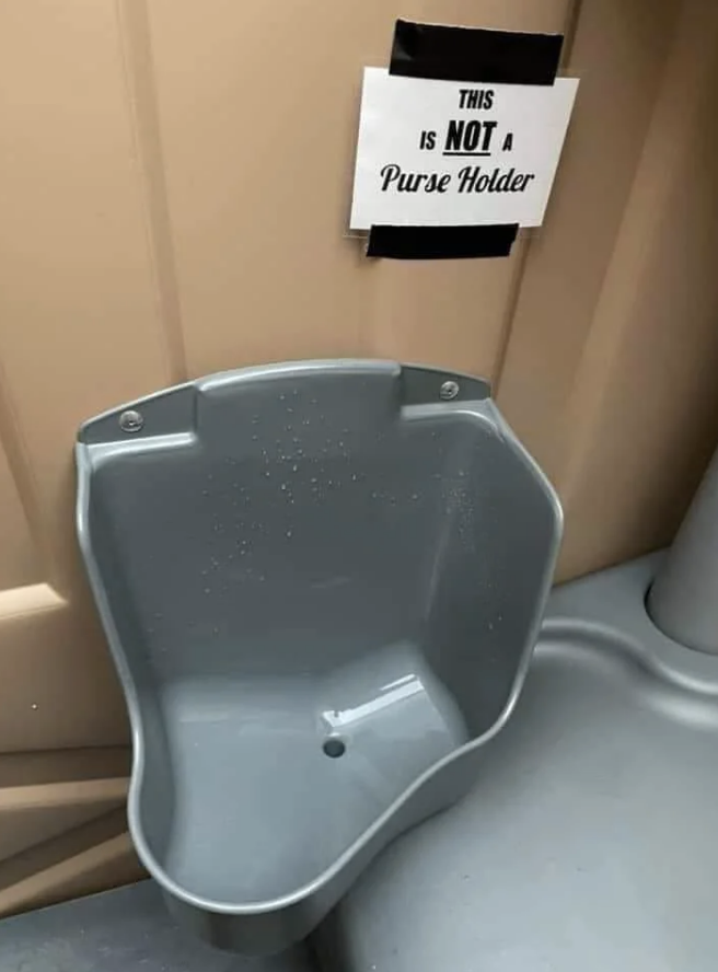 Urinal inside a portable toilet labeled: &quot;This is not a purse holder.&quot;