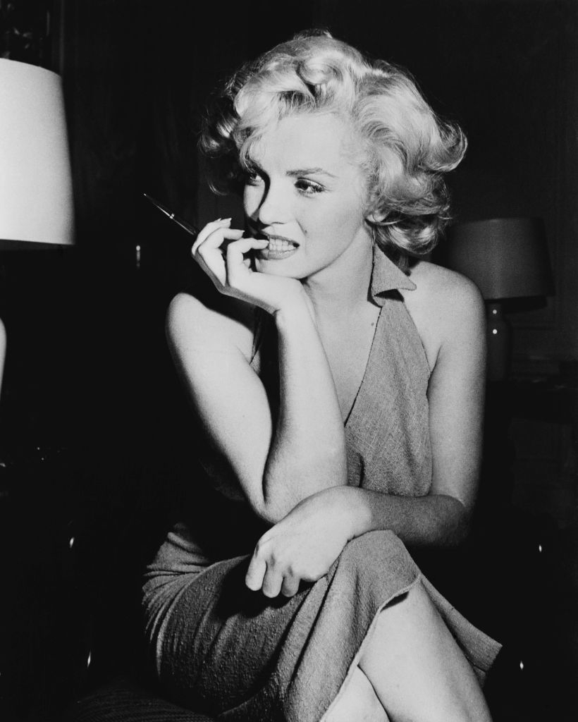 Marilyn Monroe seated in a halter dress, holding a cigarette and looking contemplative