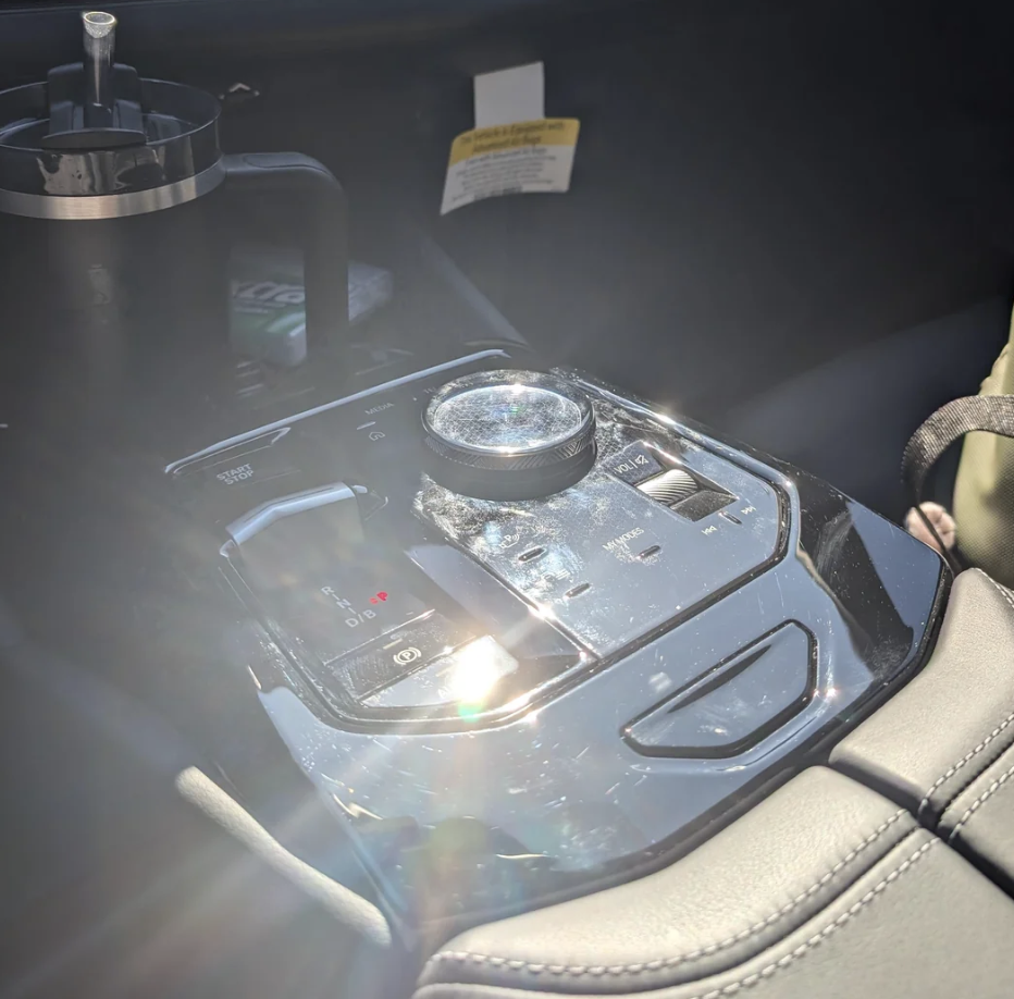 Close-up of a car&#x27;s center console with a shiny gear selector and a travel mug nearby