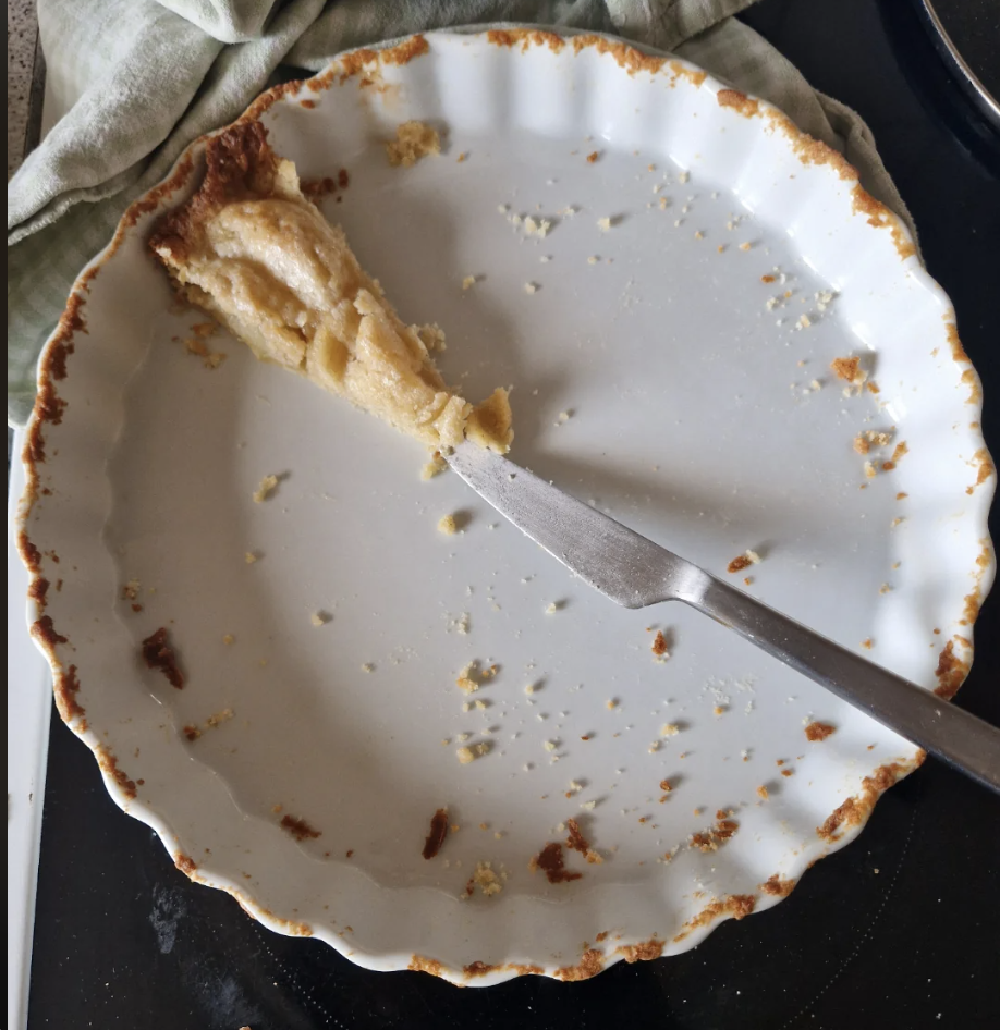 Empty pie pan with crumbs and a single slice left, knife nearby