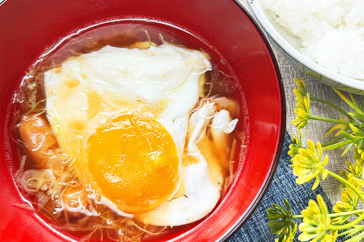 目玉焼きがのったみそ汁と白ご飯の横には小さな黄色い花が飾られている。