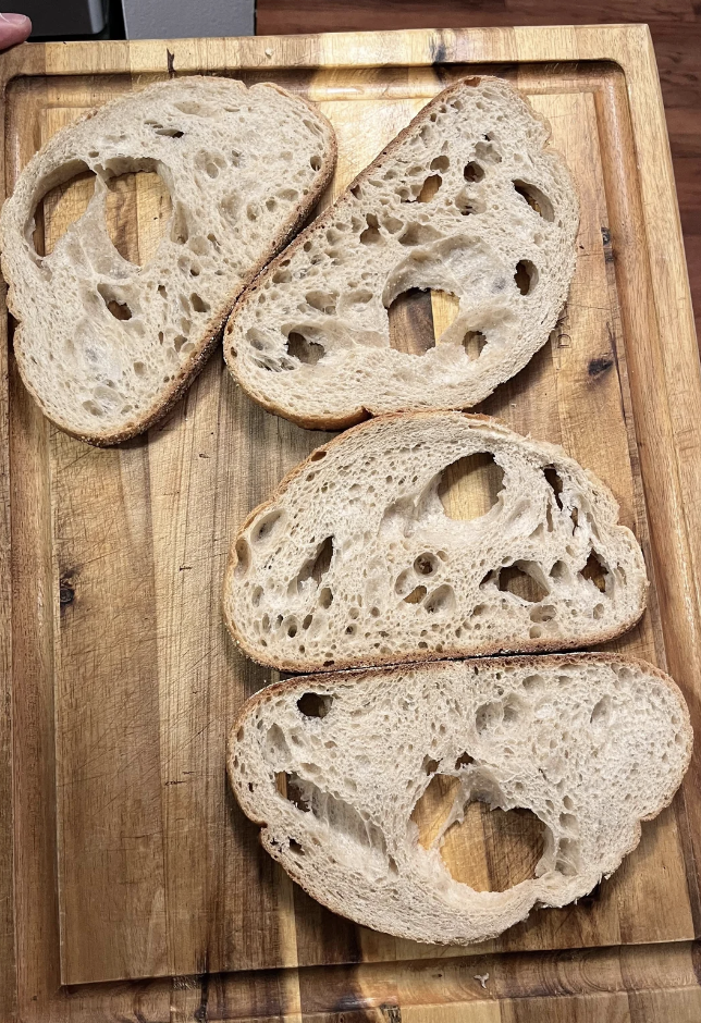 Sourdough bread slices on a wooden cutting board featuring large, irregular holes