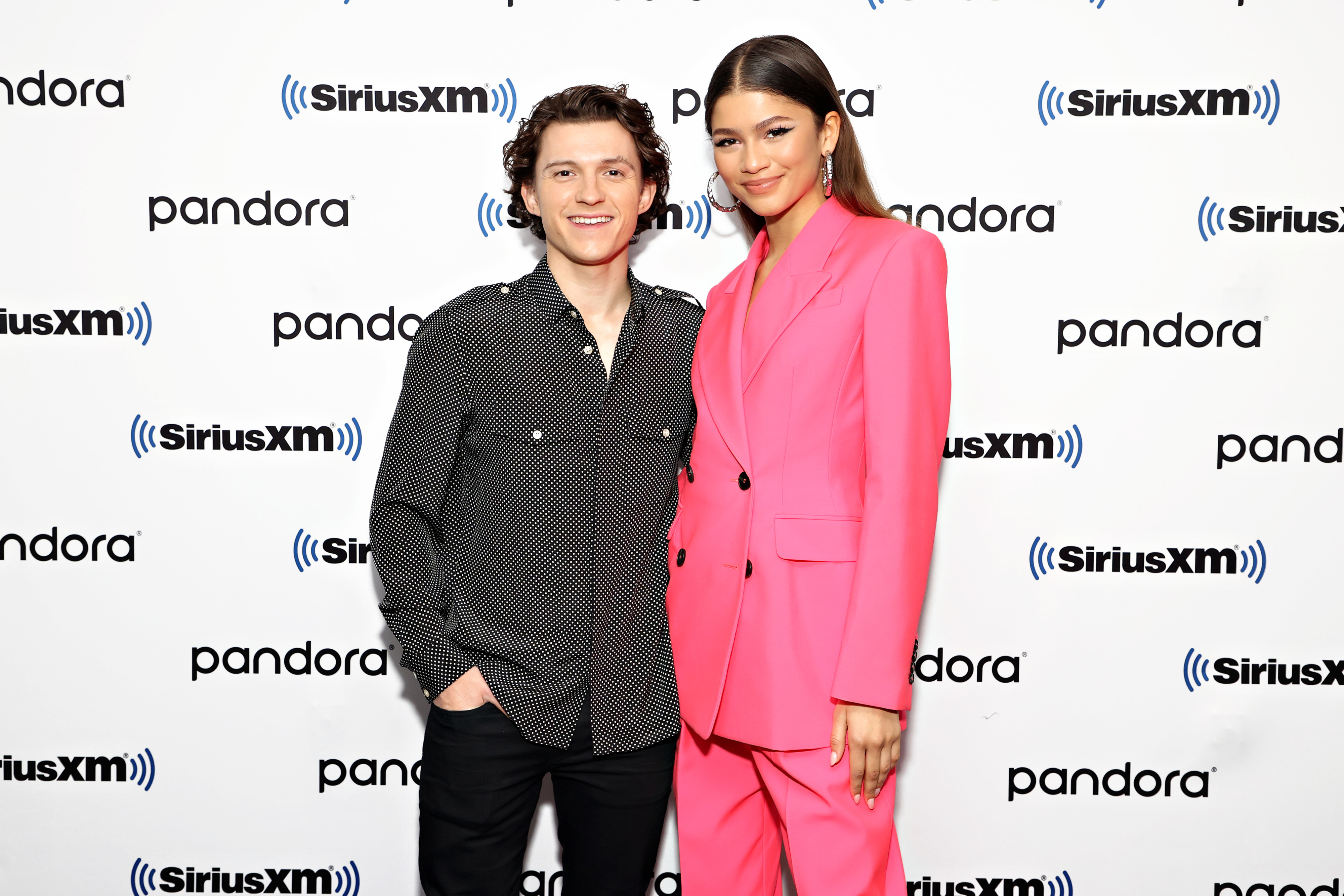 Tom Holland in a button up shirt and pants and Zendaya in a suit with hoop earrings