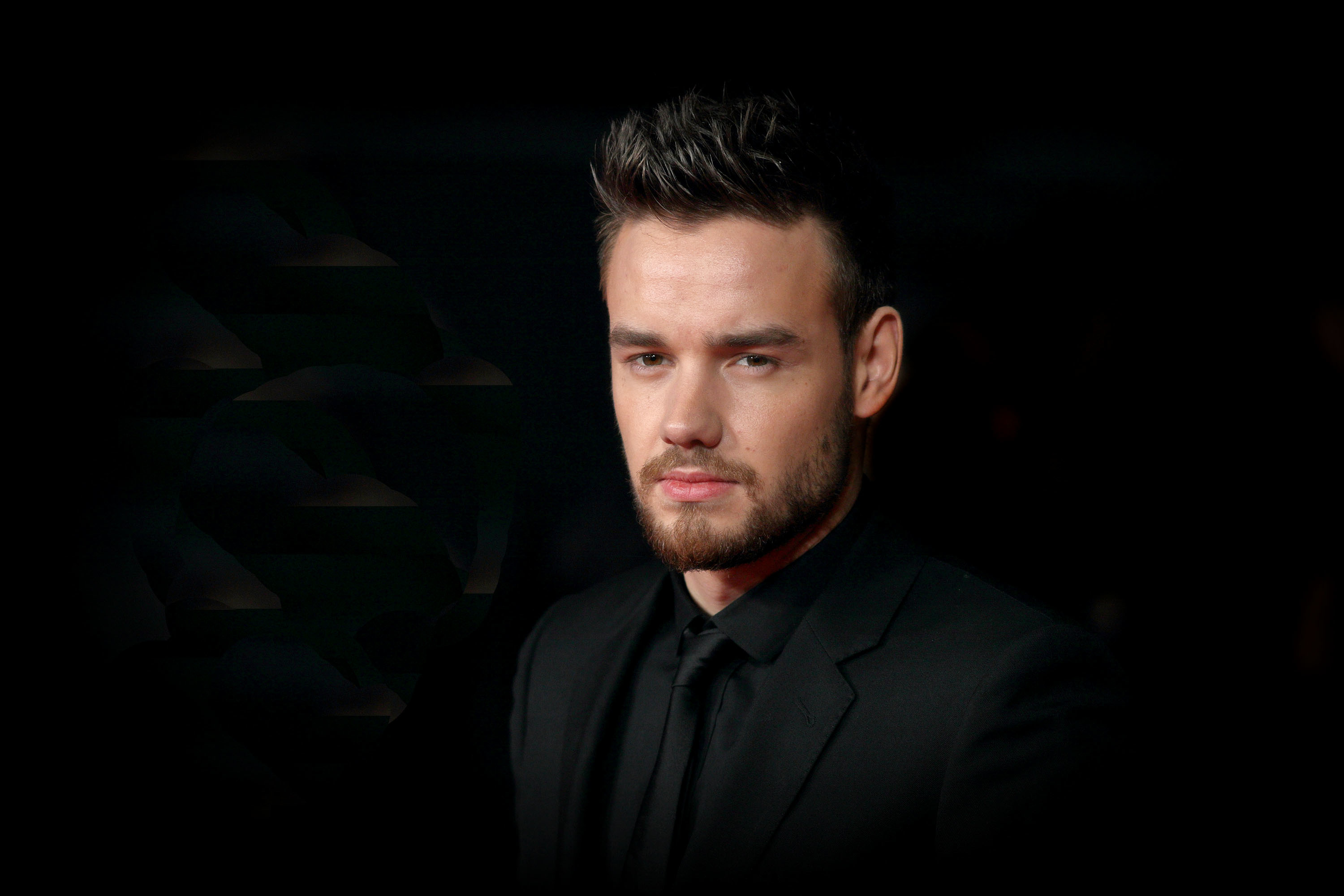 A man in a black suit poses against a dark background