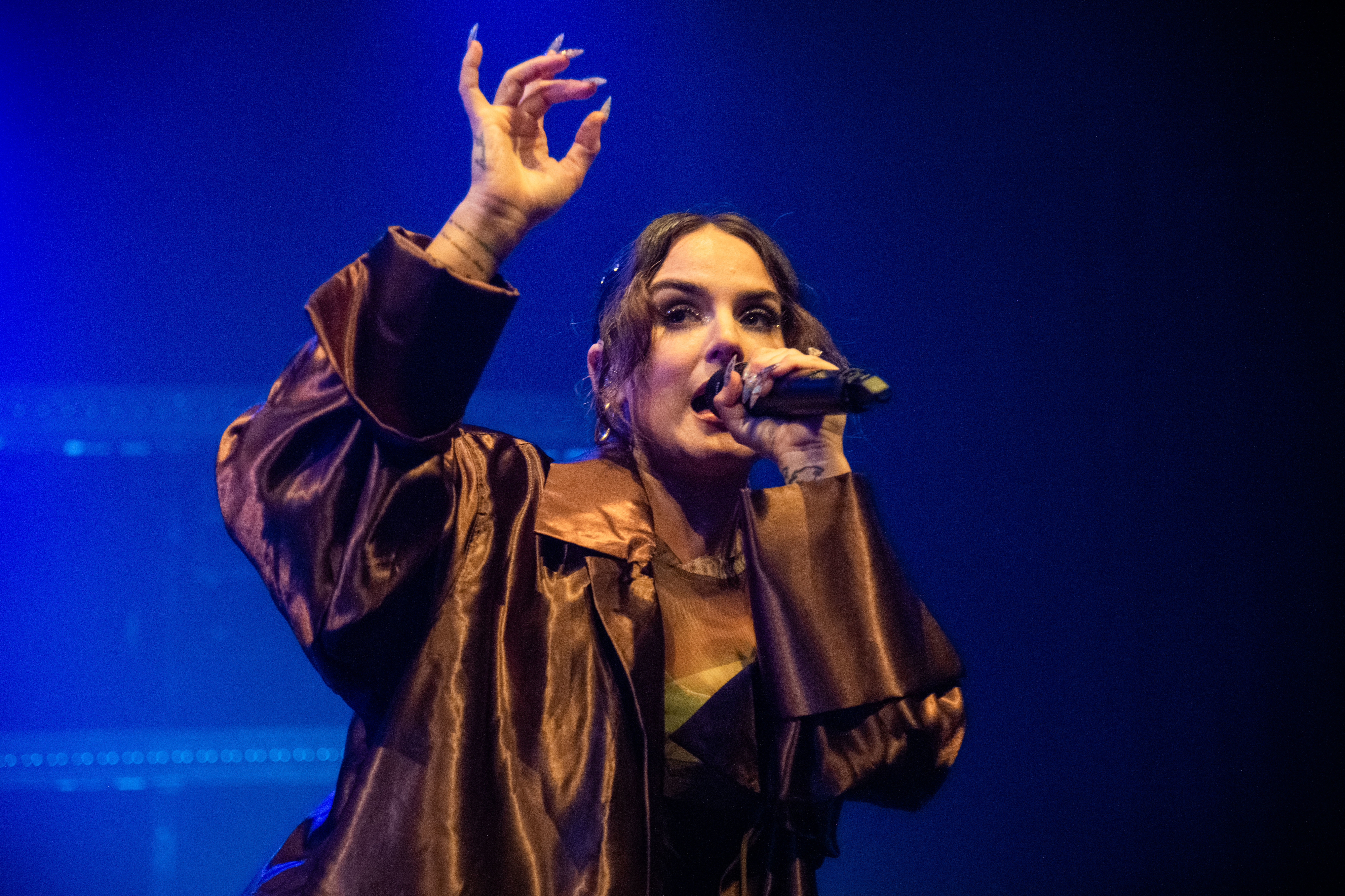 JoJo on stage wearing a glossy, oversized jacket, singing into a microphone