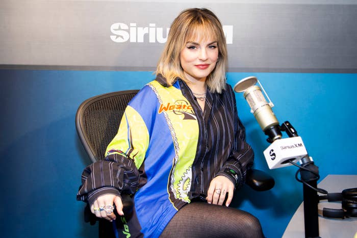 JoJo sits in a radio studio in a button up shirt with stripes and mesh tights