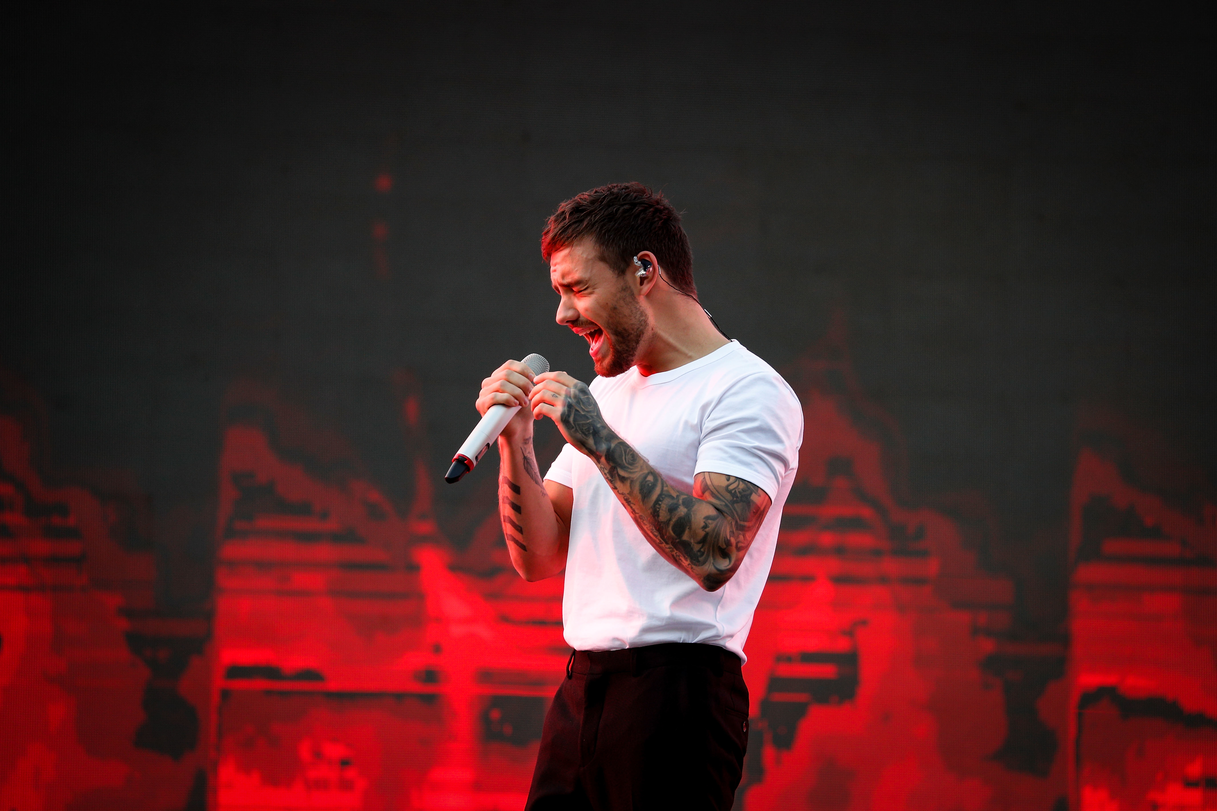 A person singing passionately on stage, wearing a white shirt and dark pants, holding a microphone with a dynamic background