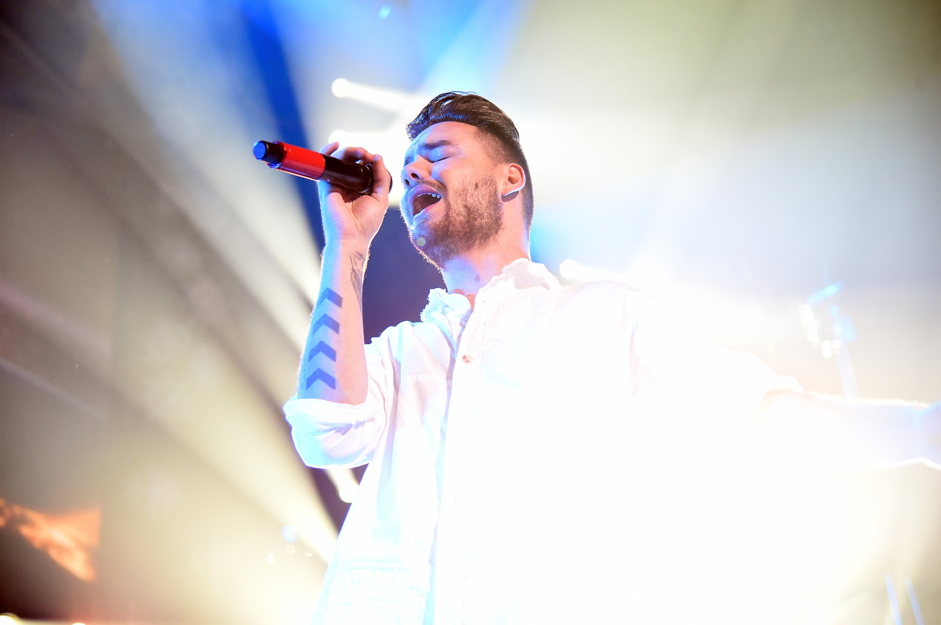 A person sings passionately into a microphone on stage, surrounded by bright lights