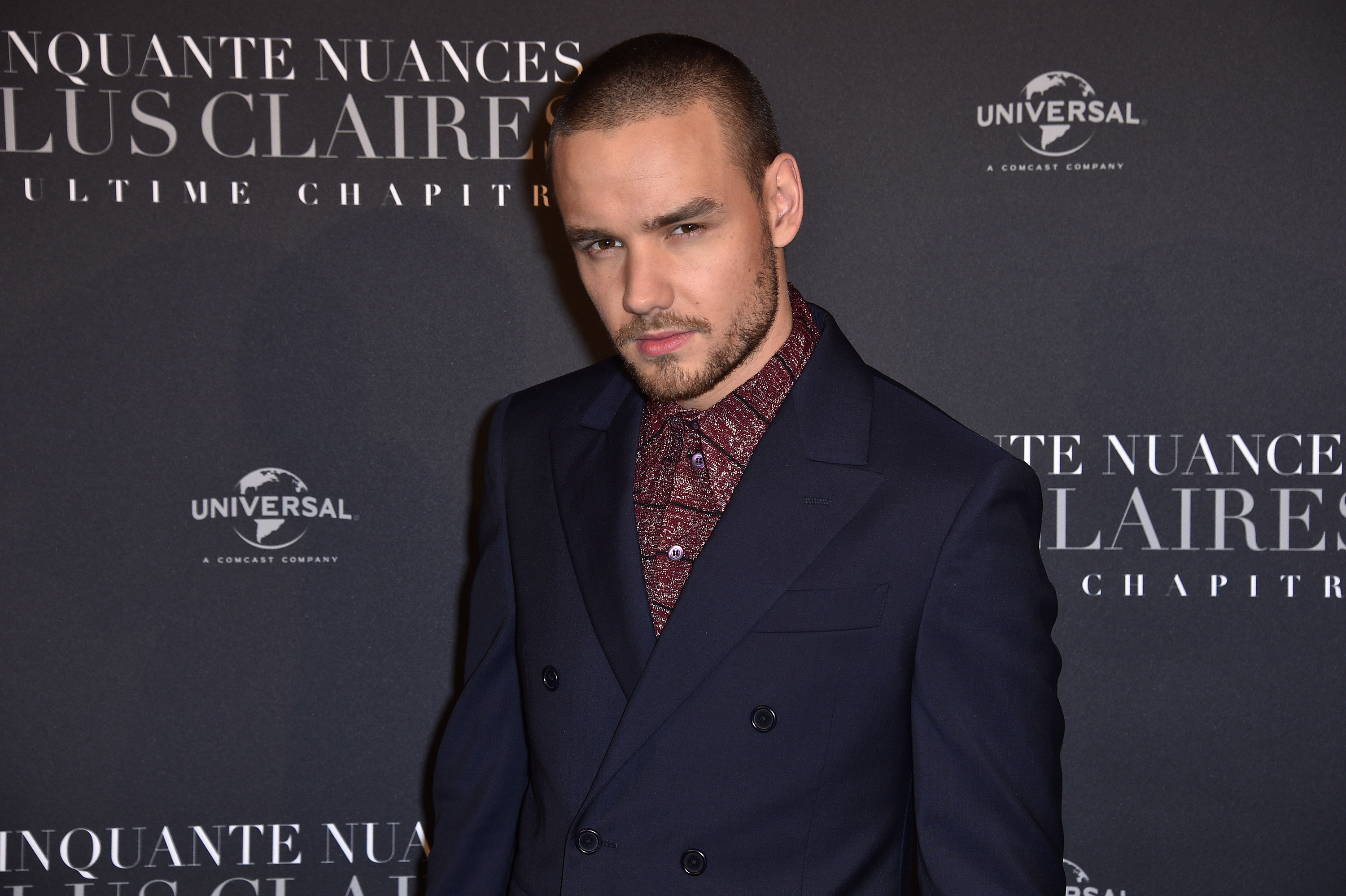 I don&#x27;t know who is in the image. A person stands in a dark suit with a patterned shirt at an event backdrop featuring text about &quot;Ultime Chapitre.&quot;