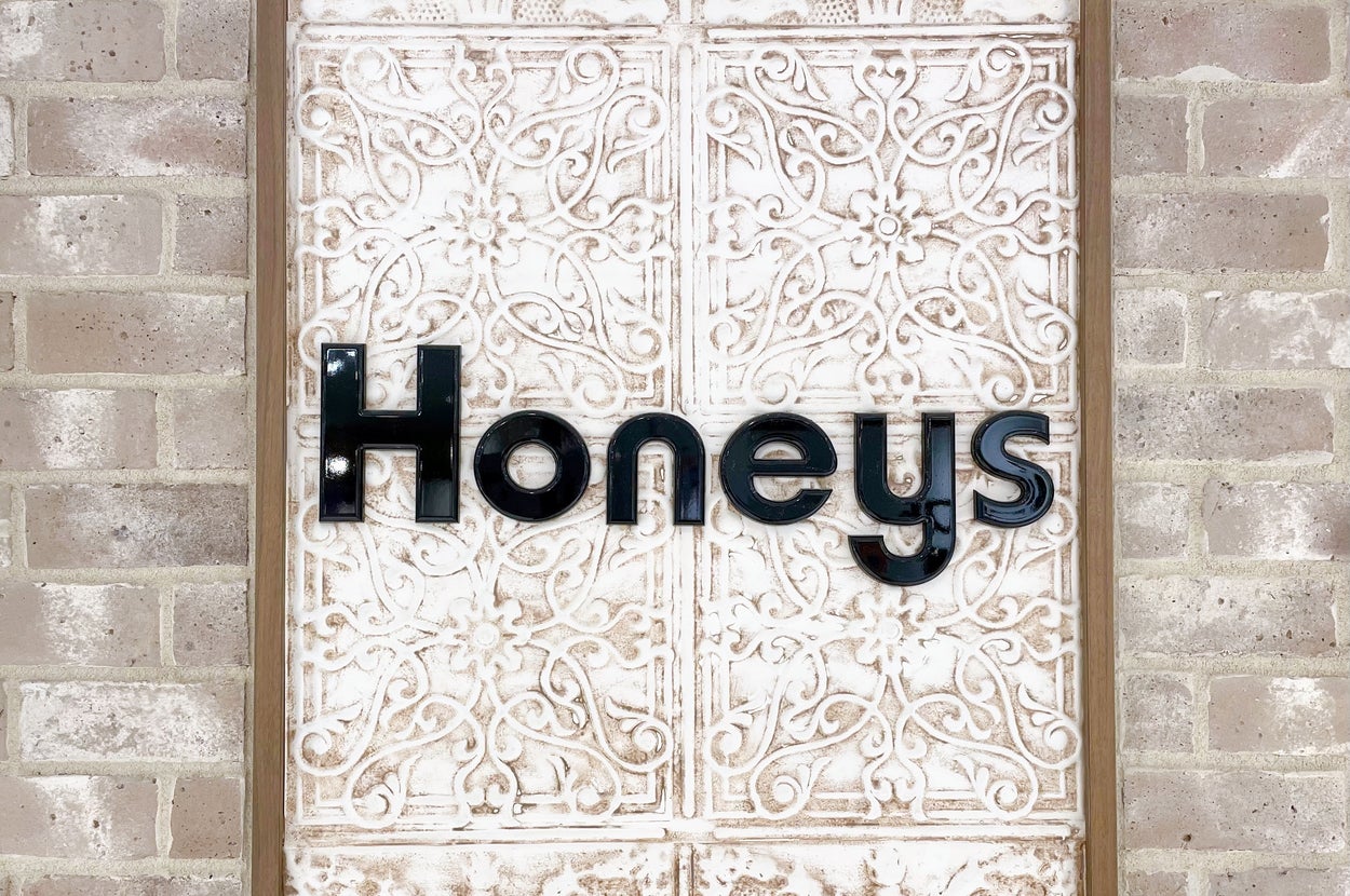 レンガの壁に取り付けられた「Honeys」という店名のサイン。背景に装飾的な模様が施されています。