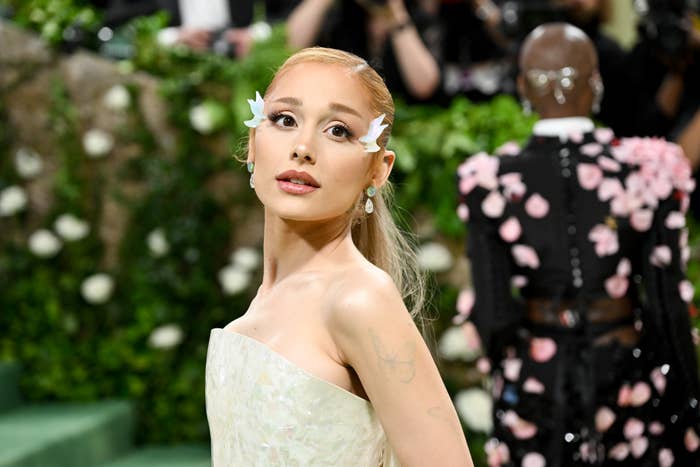Ariana Grande poses elegantly wearing a strapless gown and floral accessories on her face at an event