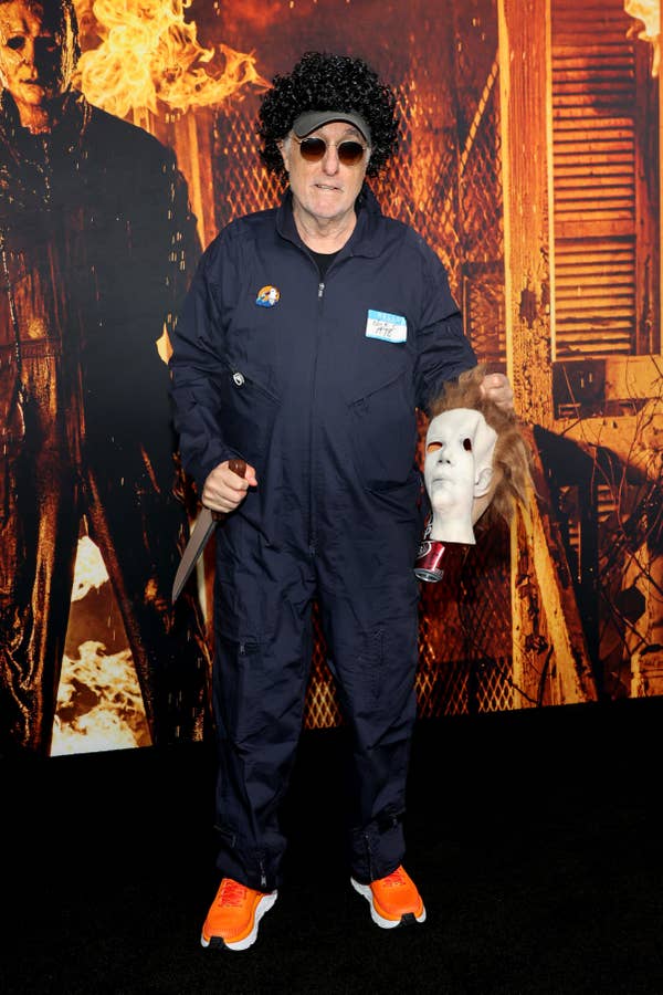 Nick Castle wearing a blue jumpsuit and orange sneakers while holding a faux knife and Michael Myers mask at the premiere of &quot;Halloween Kills&quot;