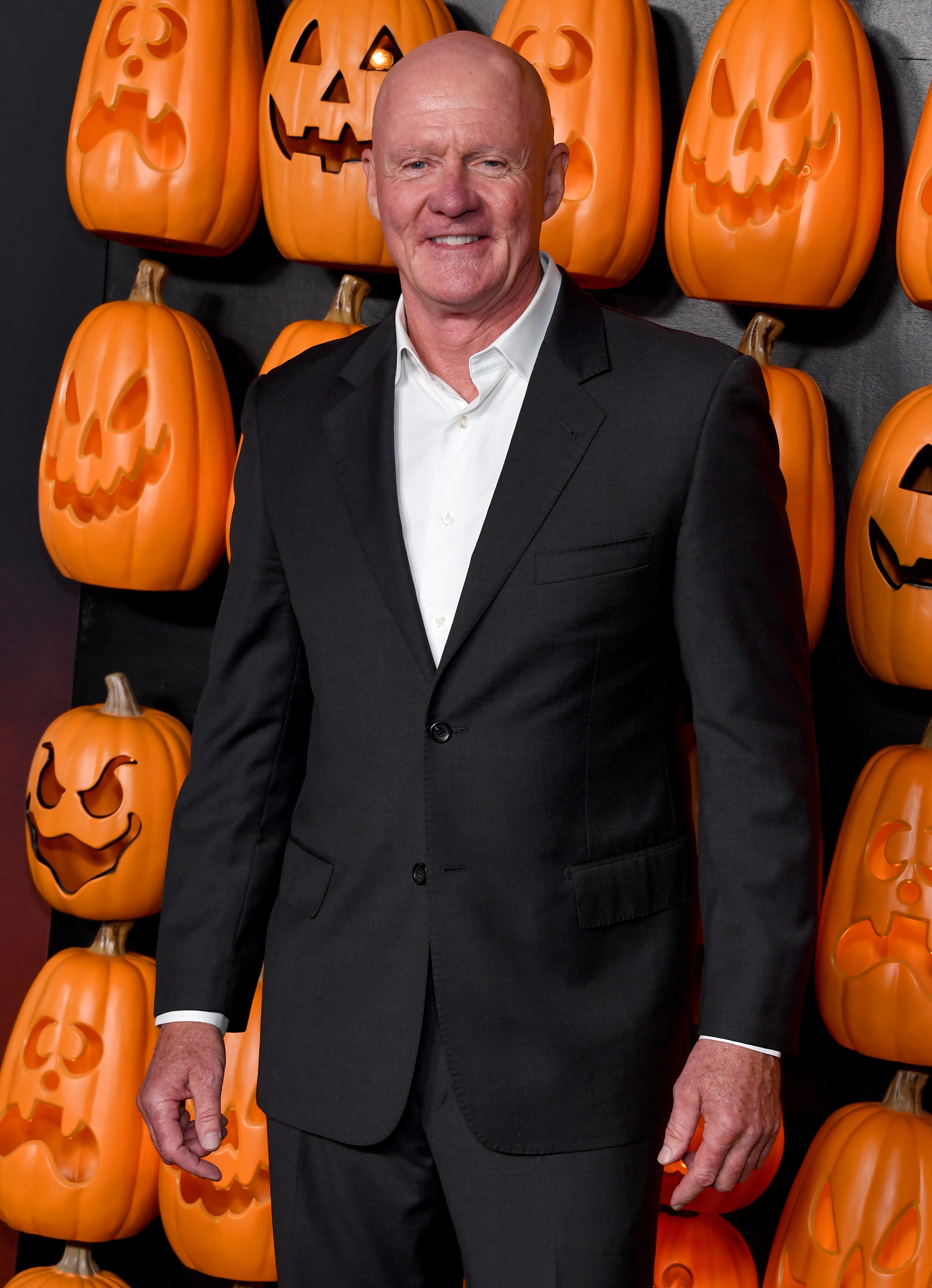 James Jude Courtney wearing a black suit in front of a background of pumpkins on the red carpet for the "Halloween Ends" premiere