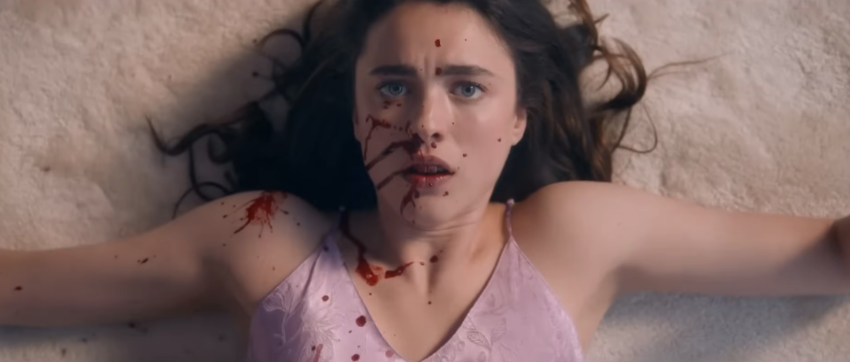 Close-up of a woman, played by Kathryn Newton, lying on the ground with blood splattered on her face, wearing a sleeveless top. Scene from a dramatic TV or movie moment