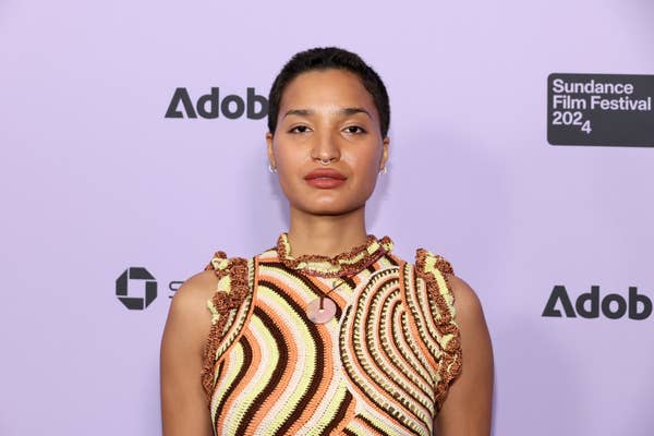 Indya Moore poses at Sundance Film Festival wearing a sleeveless patterned dress with ruffled trims, standing in front of a backdrop with &quot;Adobe&quot; and festival logos