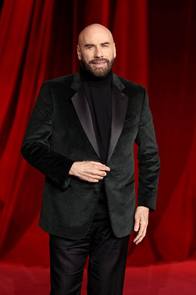 Man in formal black suit stands against red backdrop