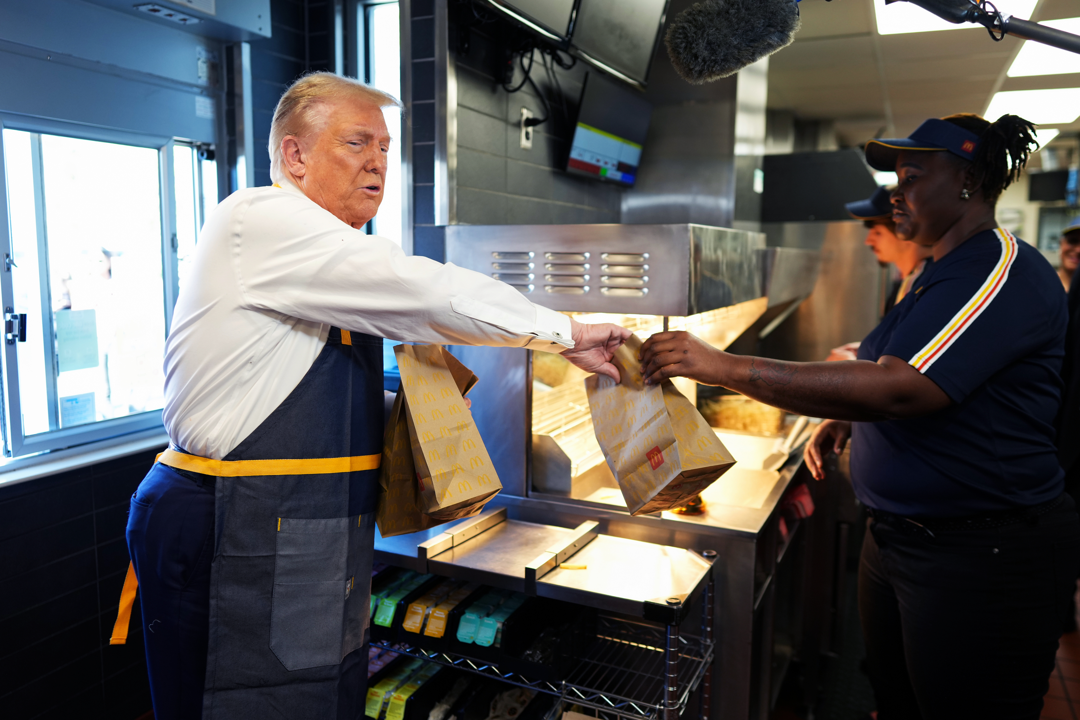 A person in an apron hands bags of food to an employee at a fast-food restaurant counter