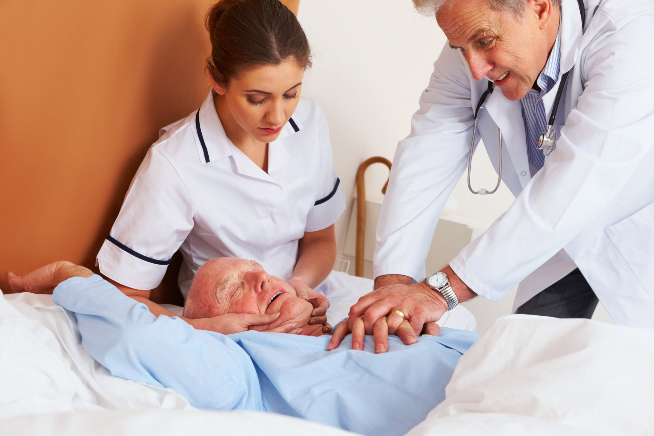 A doctor and nurse perform CPR on an elderly patient in a hospital bed