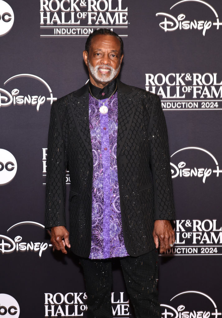 Man in patterned purple shirt and textured dark jacket at Rock &amp;amp; Roll Hall of Fame Induction 2024 event backdrop