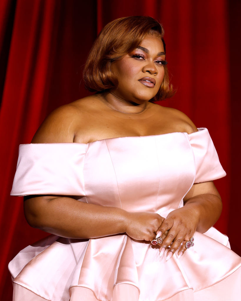 I don&#x27;t know who this is. Woman in an elegant, off-shoulder gown poses in front of a curtain backdrop