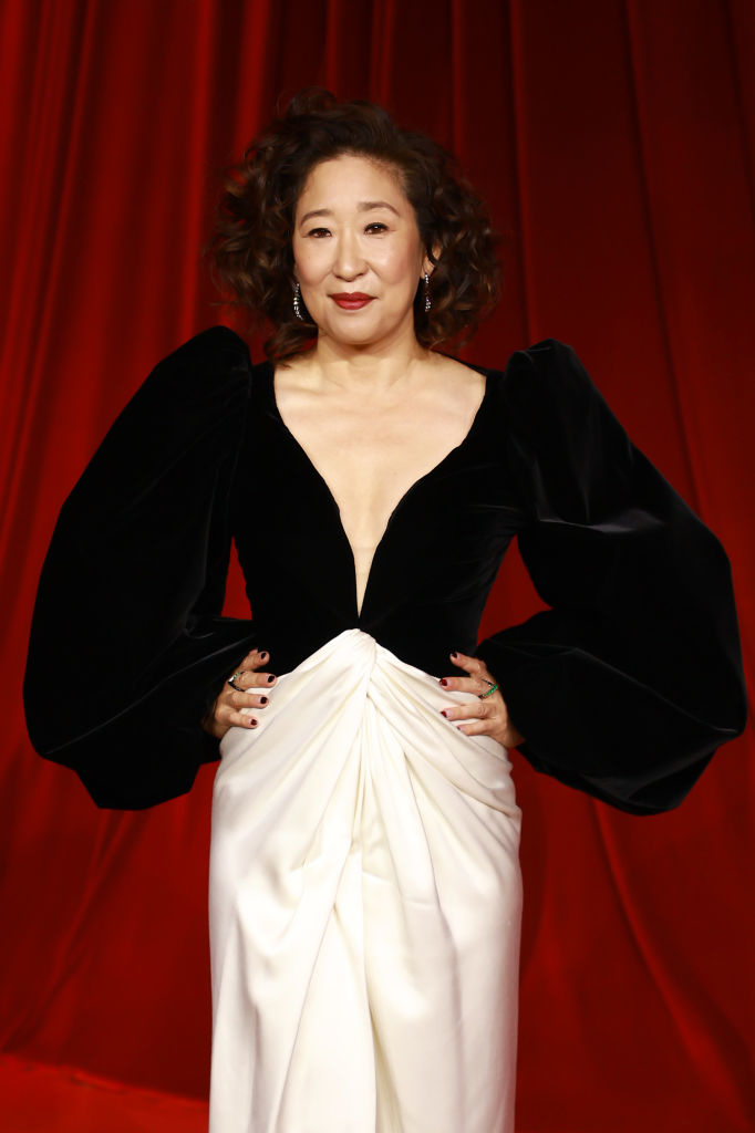 A person is posing on the red carpet wearing a black gown with large sleeves and a white skirt