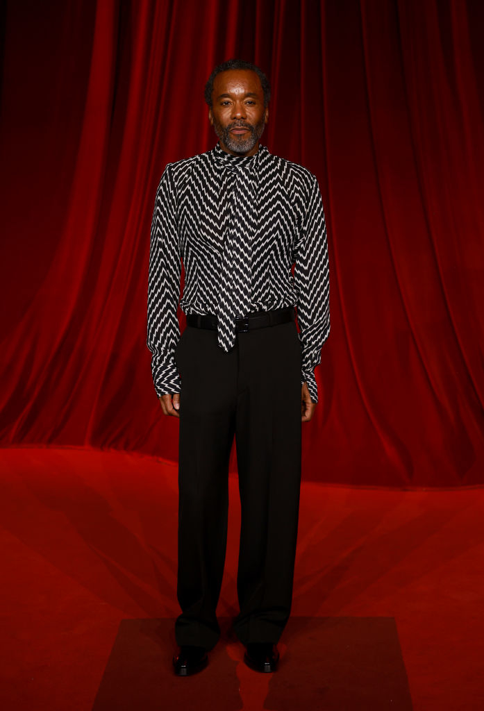 A person on a red carpet wears a patterned shirt and black pants