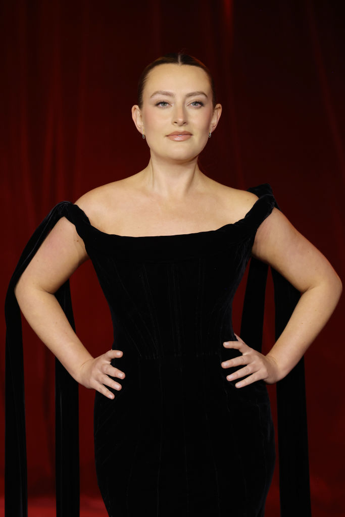 I don’t know who this person is. The individual is on a red carpet wearing an elegant, off-the-shoulder black gown with ribbon details