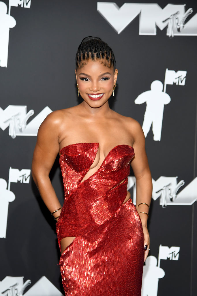 Halle Bailey on a red carpet in a strapless textured gown with a cutout, smiling and posing in front of MTV logos