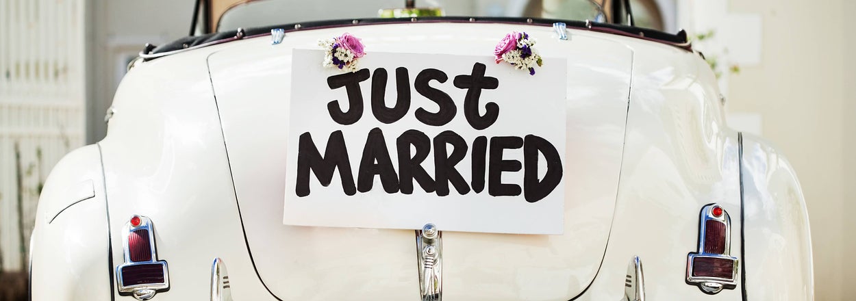 "Just Married" sign on the back of a classic convertible car with cans trailing behind