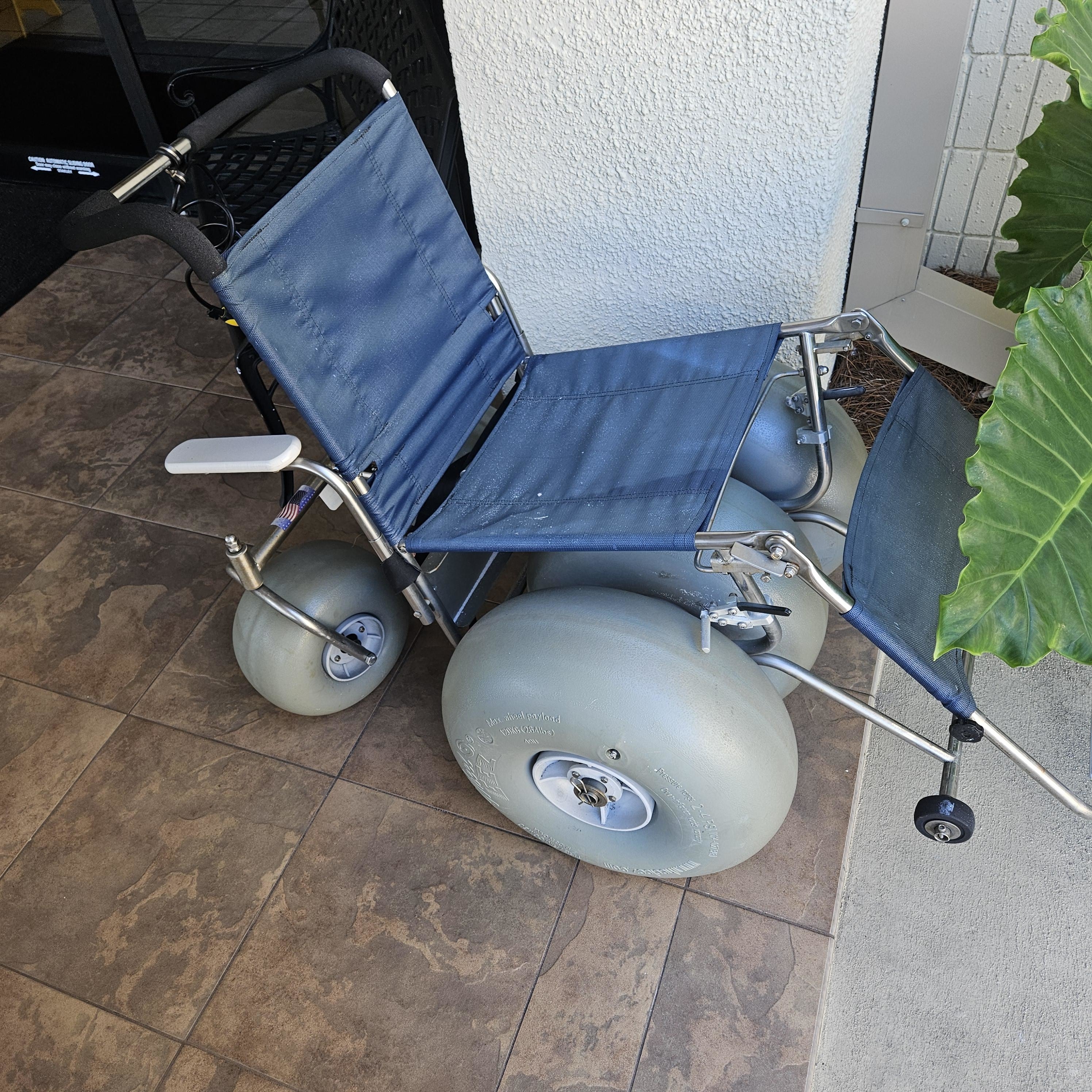 Wheelchair with large inflatable tires designed for beach use, near a building entrance