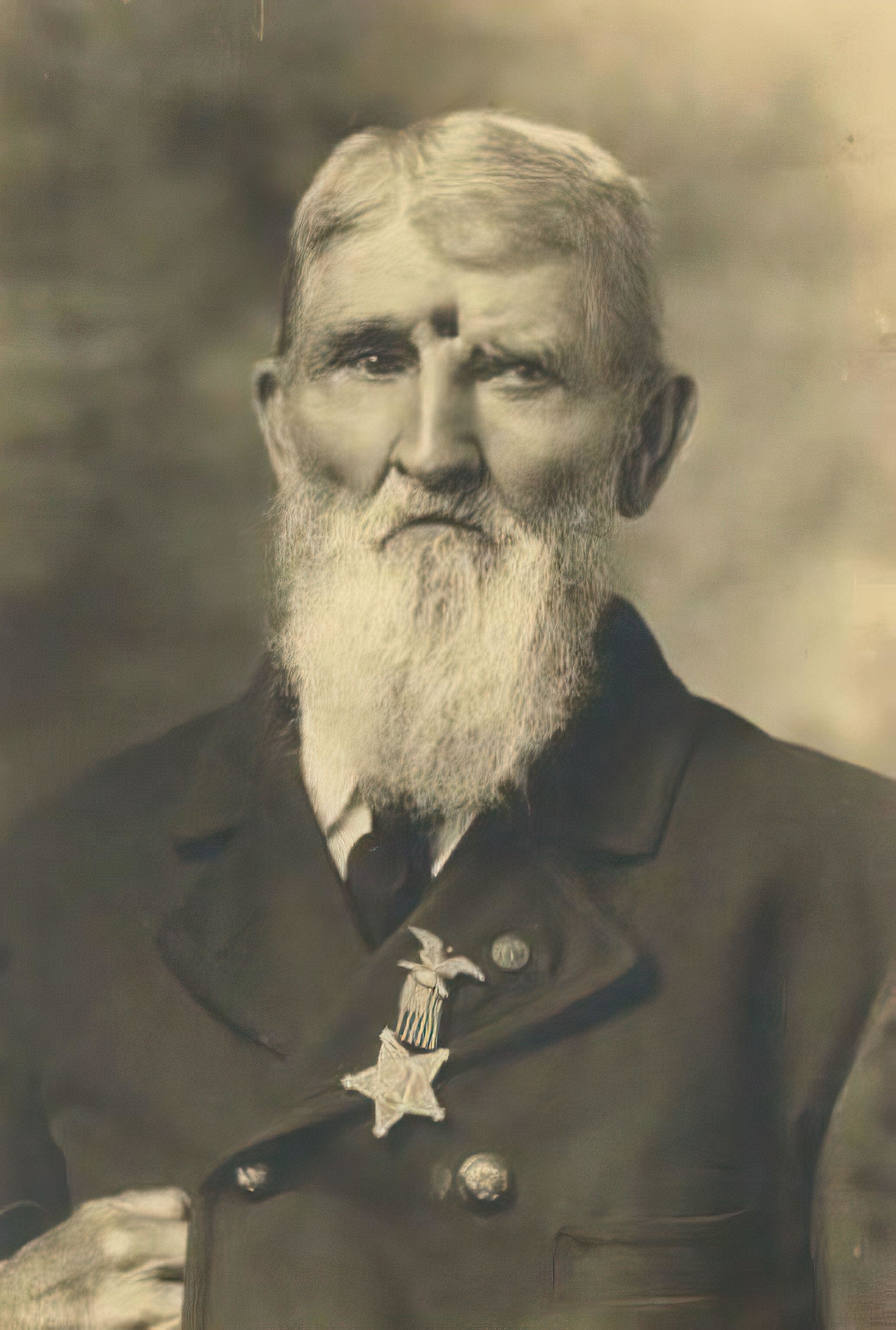 An elderly man with a long white beard, wearing a suit with a star-shaped medal pinned to his chest. Unknown identity