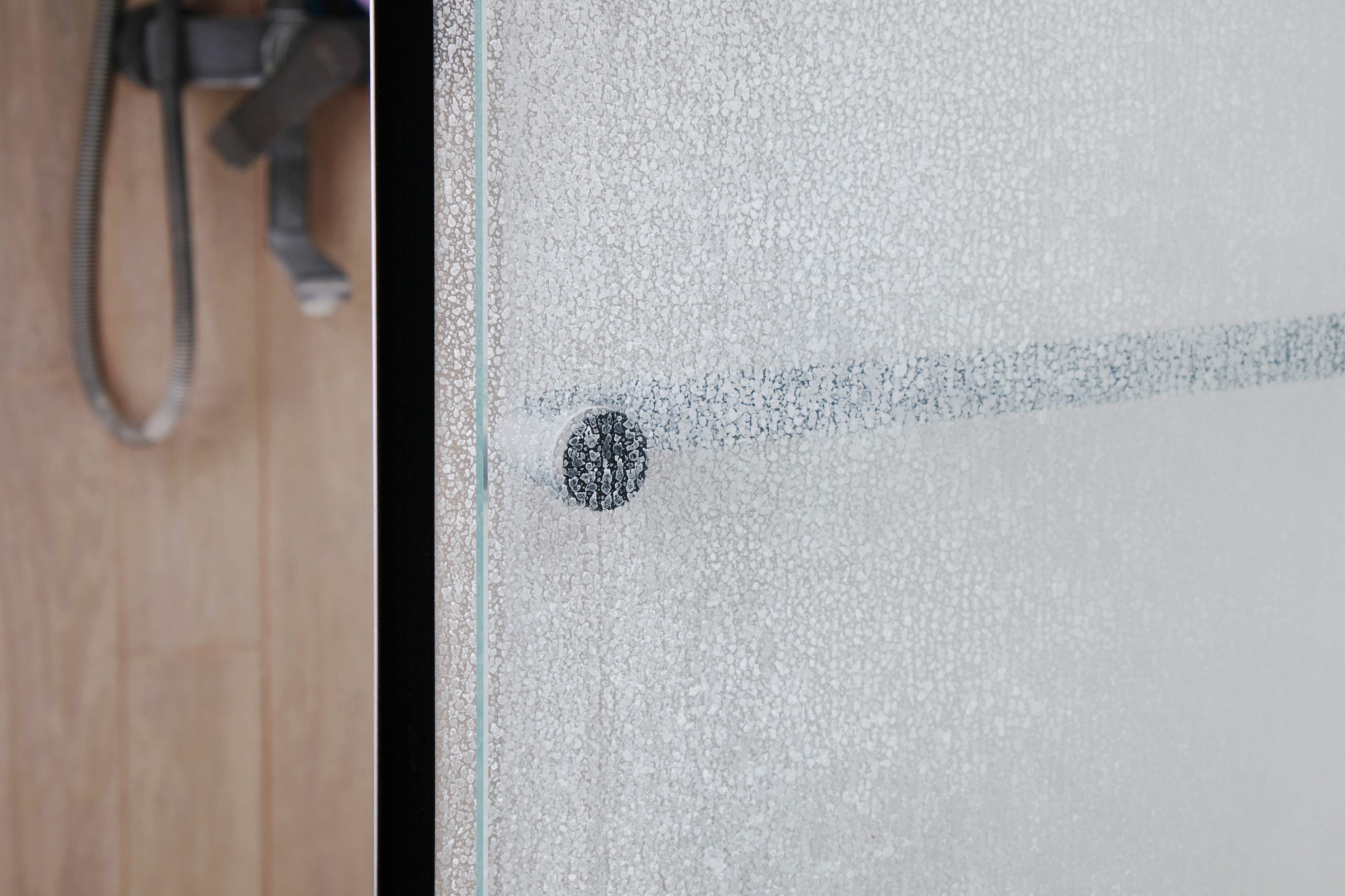 Frosted shower door with a handle; a glimpse of a showerhead is visible in the background