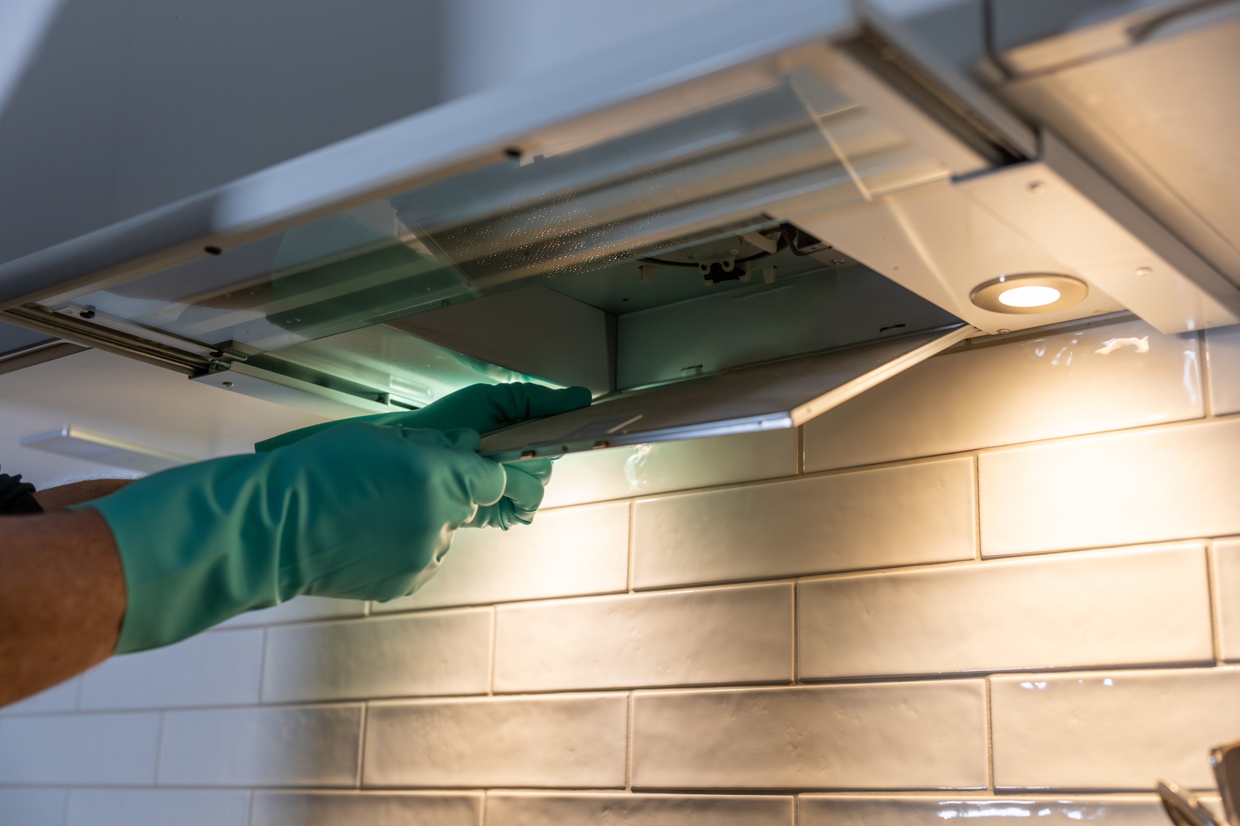 Person wearing rubber gloves removes filter from under-cabinet range hood in kitchen