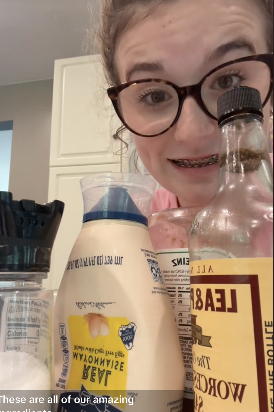 Addie in glasses and braces smiles with bottles and a jar of ingredients in front