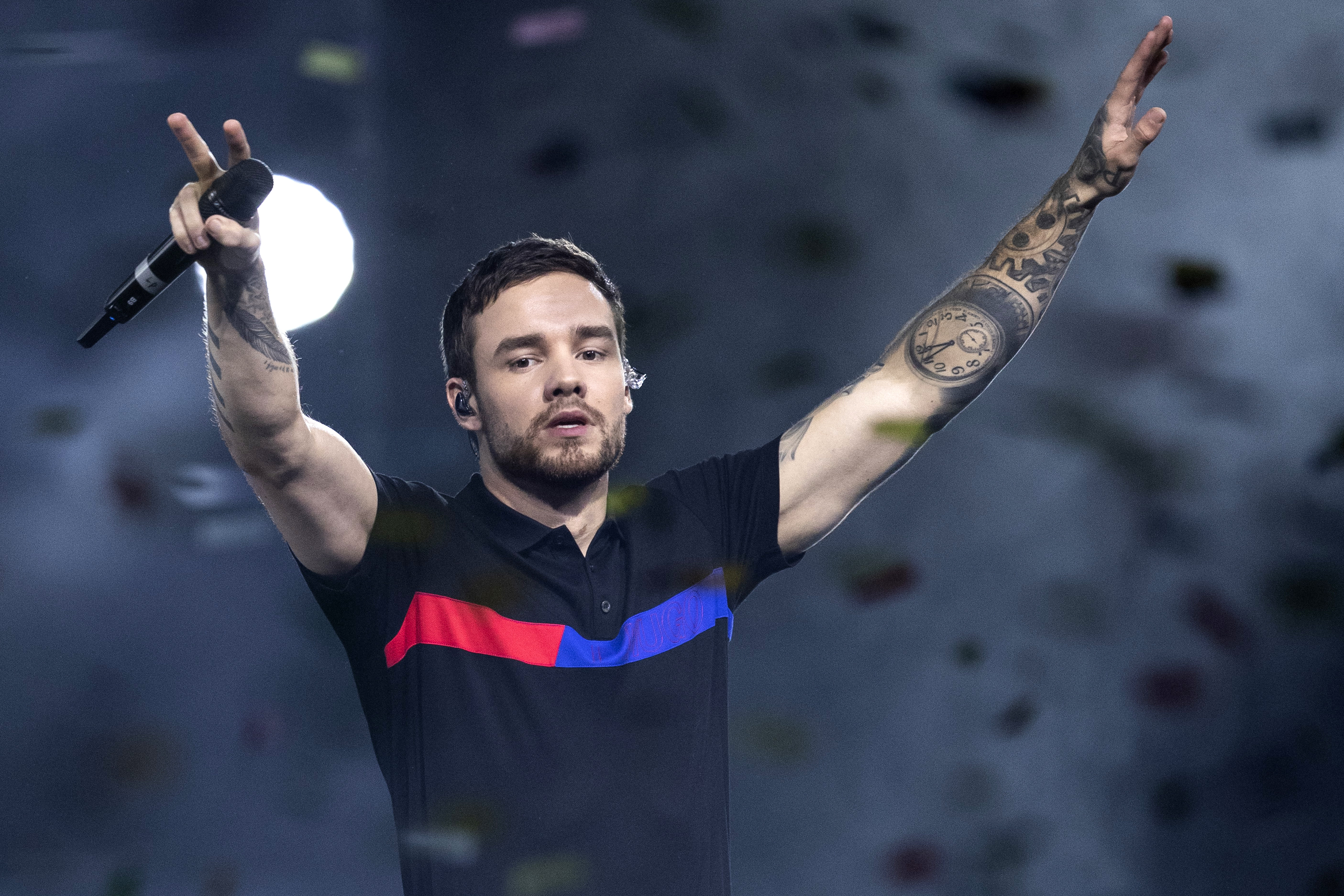 Liam Payne performing on stage raises his arms, holding a microphone, surrounded by falling confetti