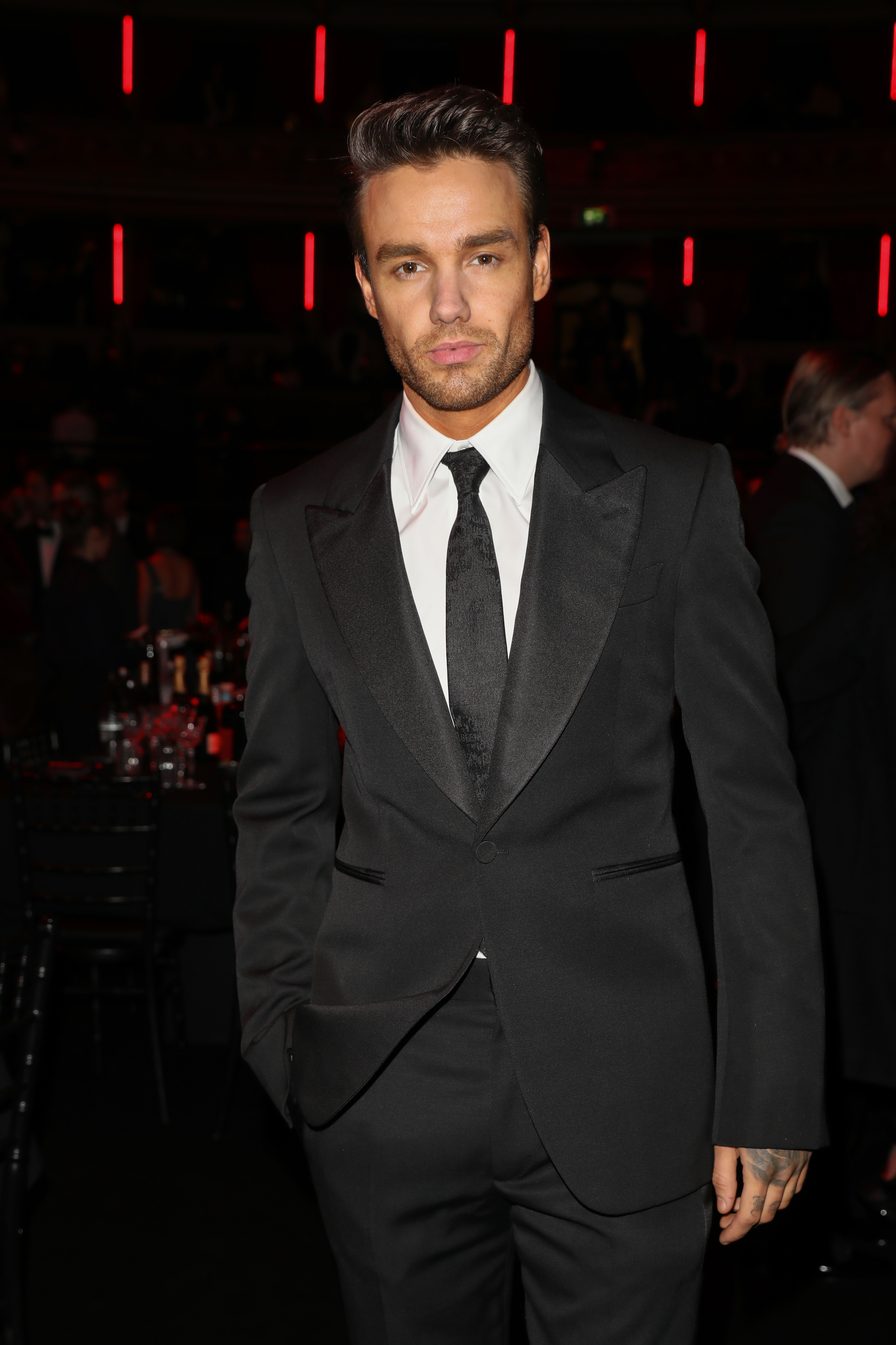 Liam Payne in a formal suit with a tie at a black-tie event in a dimly lit venue