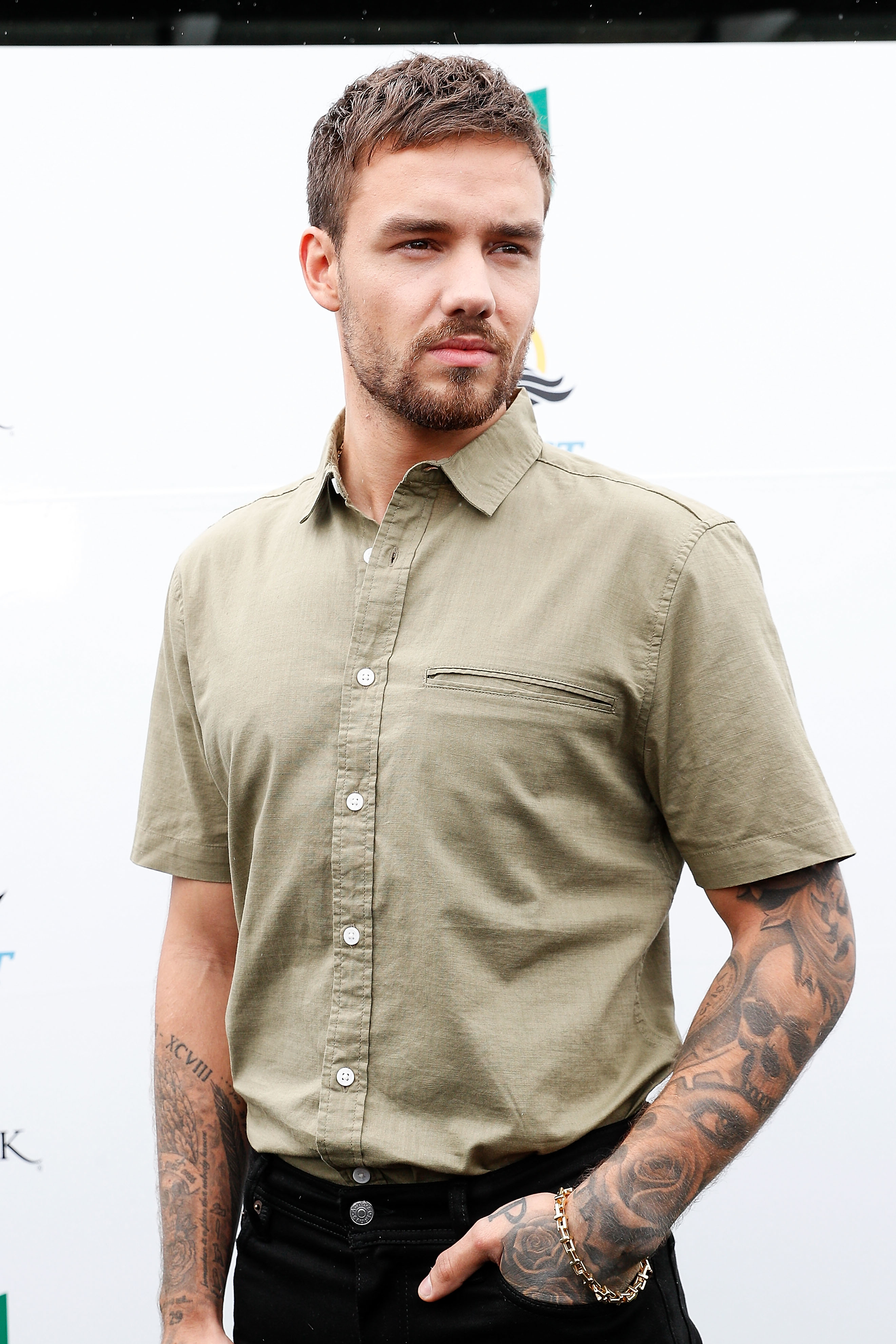 Liam Payne with tattoos wearing a short-sleeve button-up shirt poses confidently, looking to the side