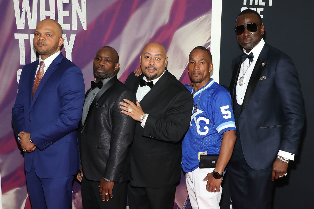 Five men in suits and formal wear, one wearing a sports jersey, pose together at a red carpet event