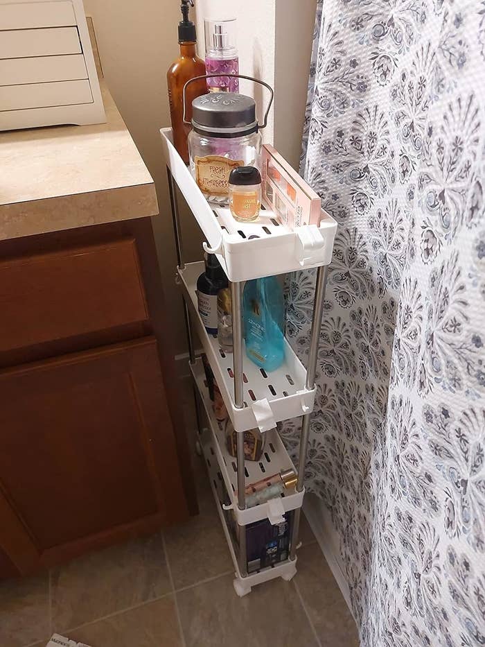 Bathroom corner with a white tiered storage organizer holding toiletries like lotions, jars, and bottles