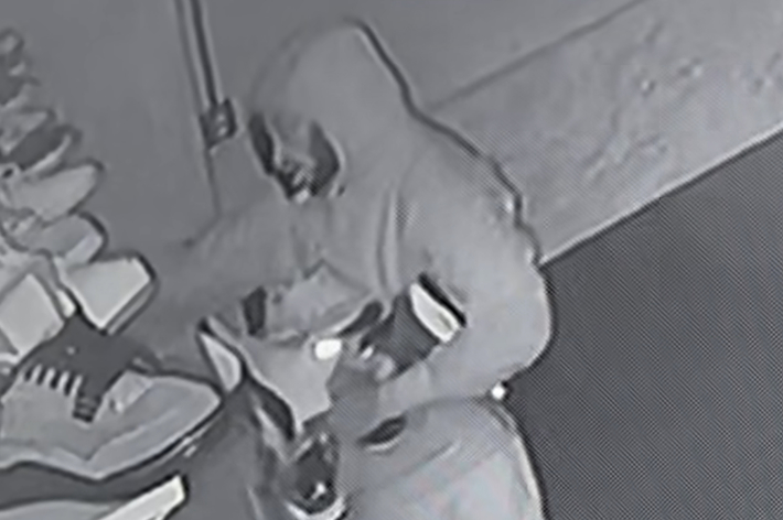 フードをかぶった人物が靴を見ている監視カメラ映像。