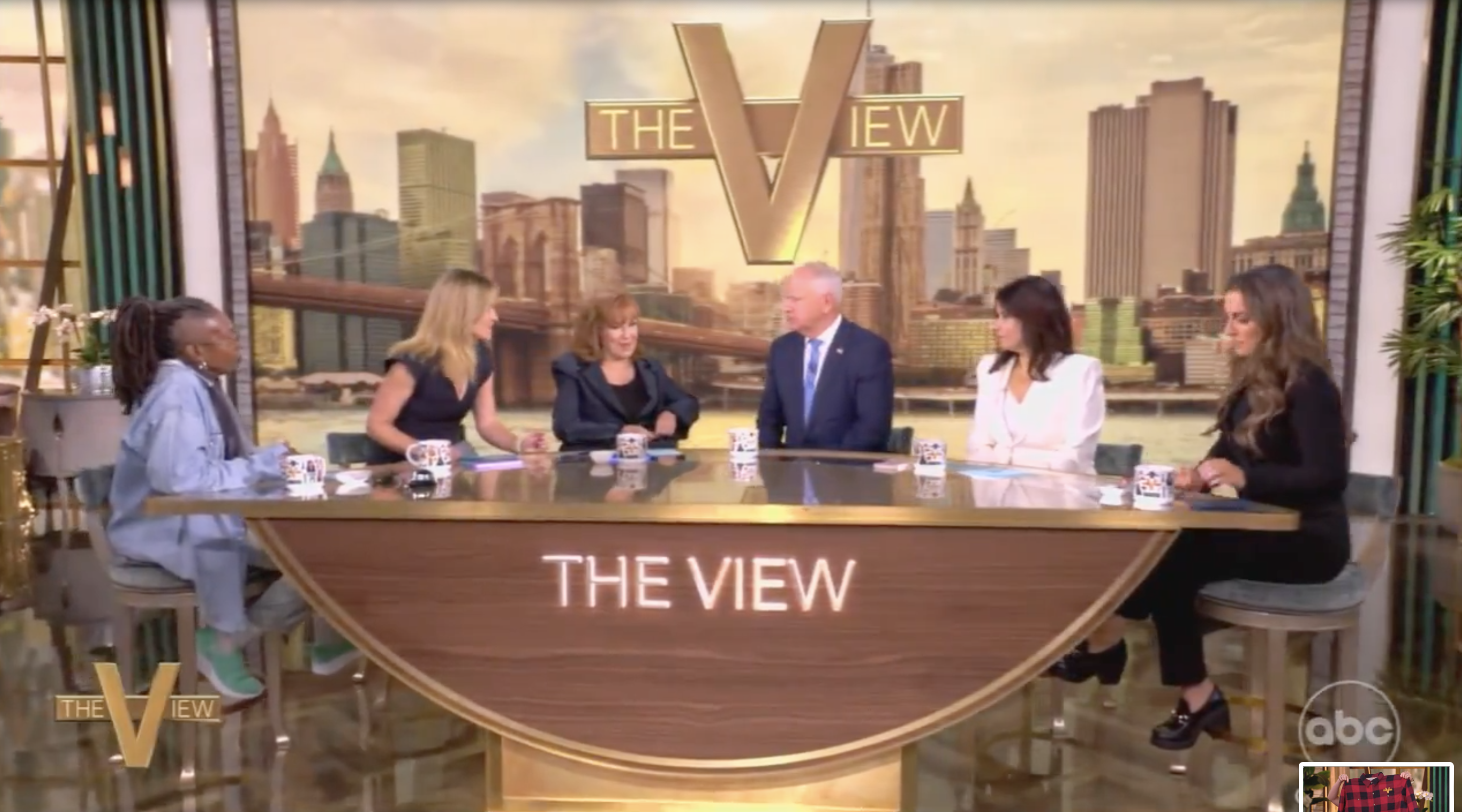 Group of six people seated at a table on the set of &quot;The View,&quot; with New York City skyline backdrop