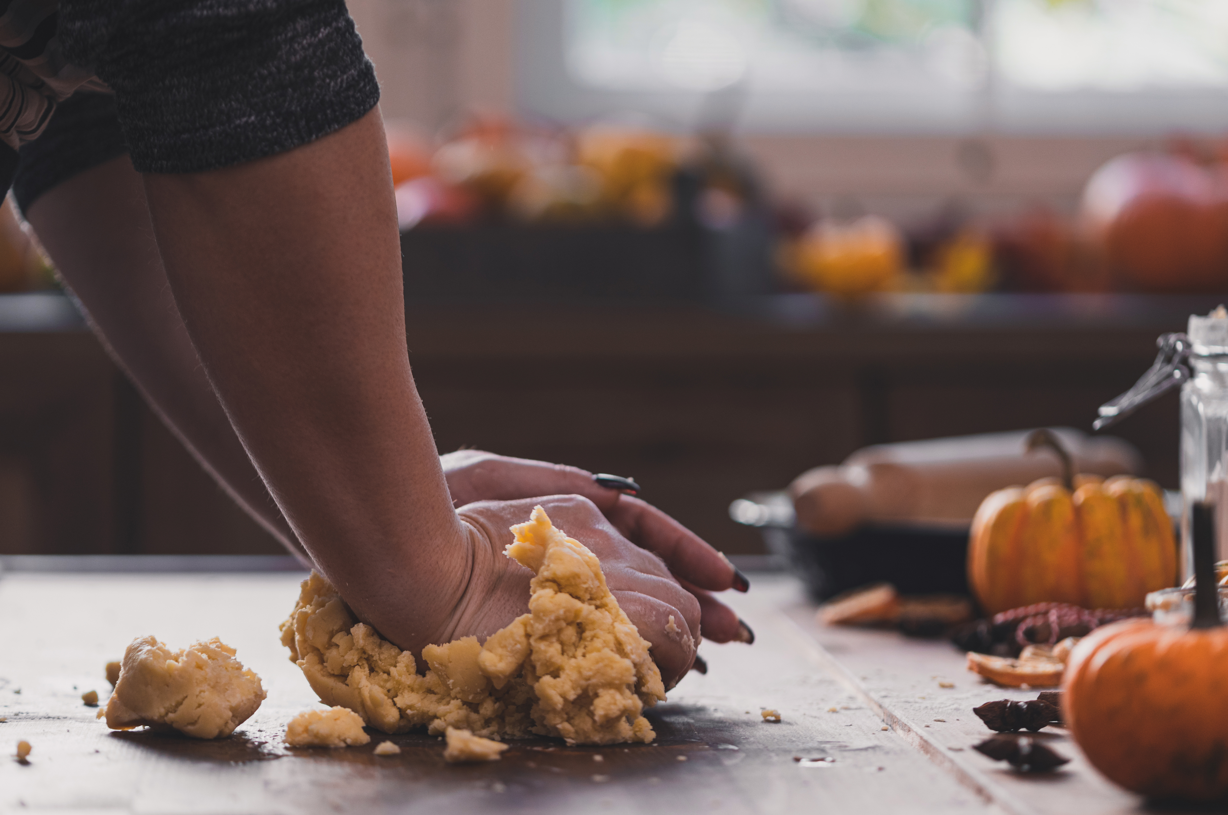 Person kneading dough on a kitchen counter with small pumpkins and autumn decor in the background