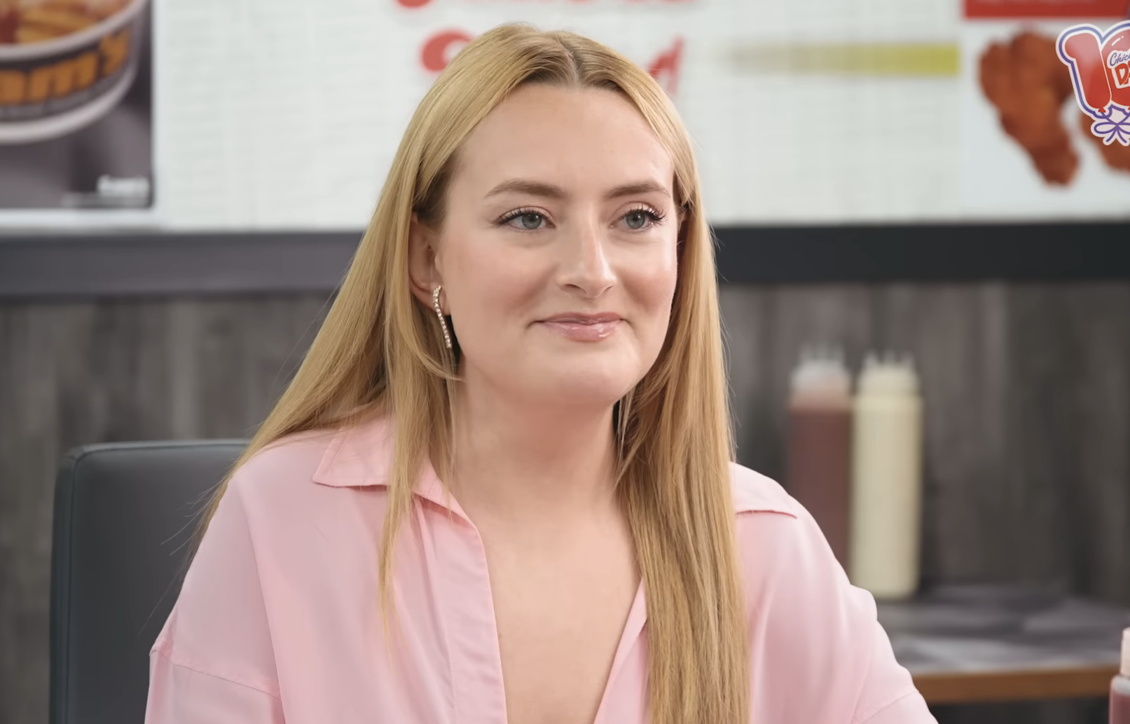 Amelia Dimoldenberg during an interview for "Chicken Shop Date" on YouTube, sitting at a table with condiments visible in the background