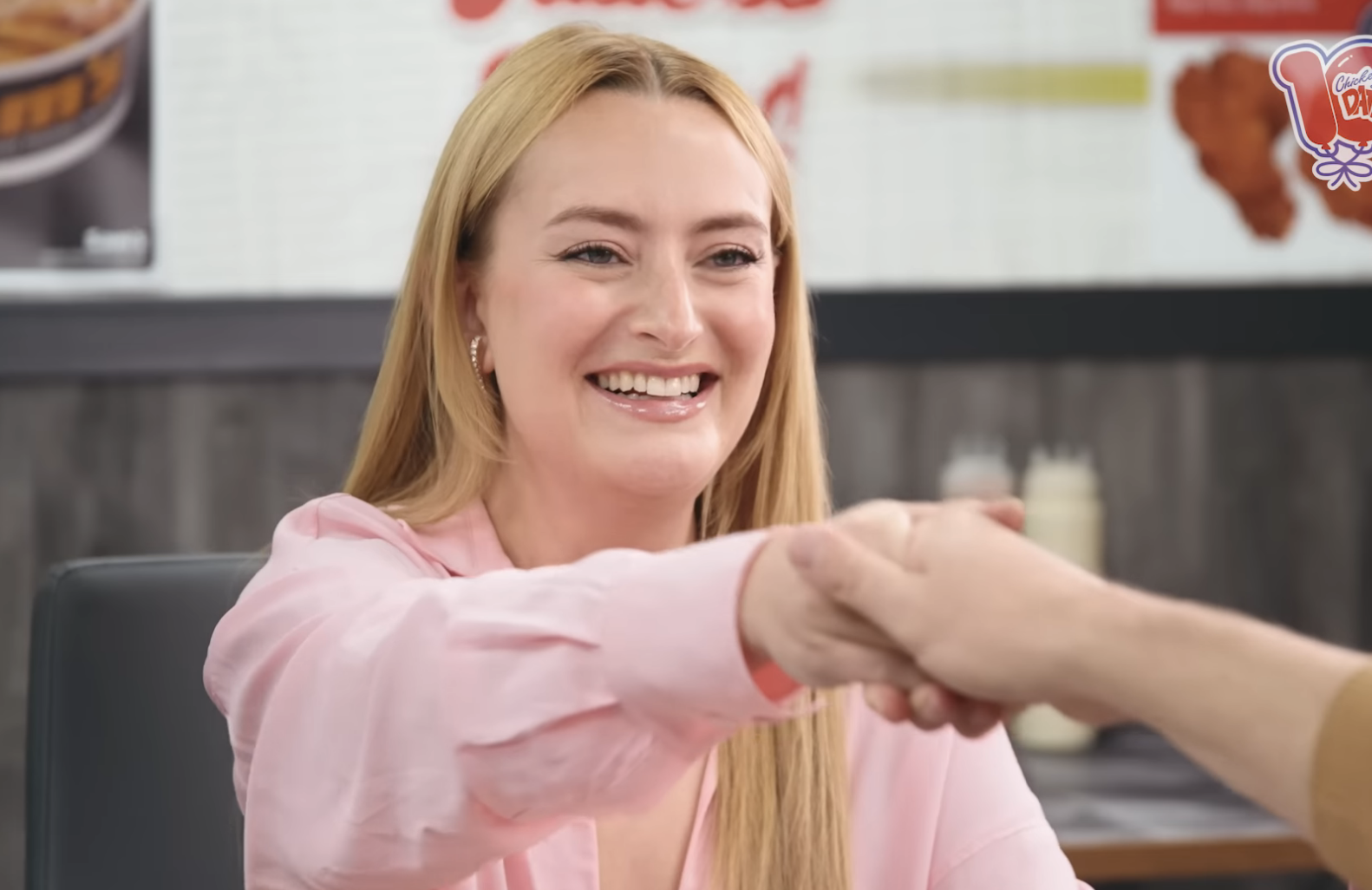 Amelia Dimoldenberg shakes hands with a guest on "Chicken Shop Date." YouTube interface with video details shown